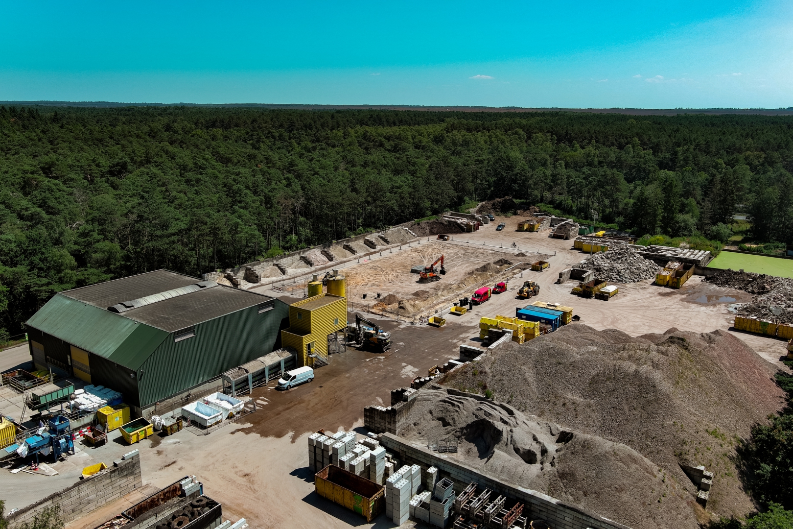 Luchtfoto van Recycling Oldebroek midden in het bos, met de groene loods, gele containers en bergen grond en puin