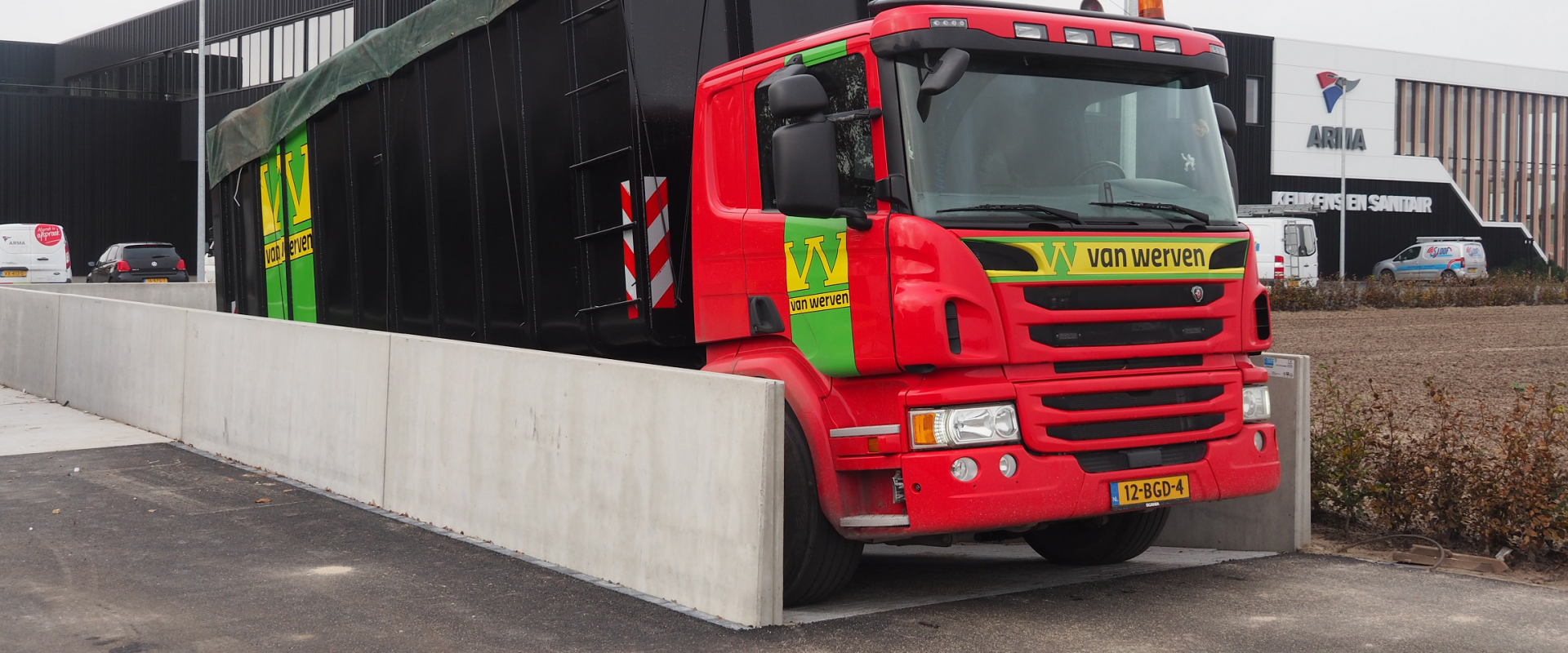 Vrachtwagen van Van Werven met afzetcontainer op de betonnen laadvloer bij het pand van Arma Keukens en Sanitair