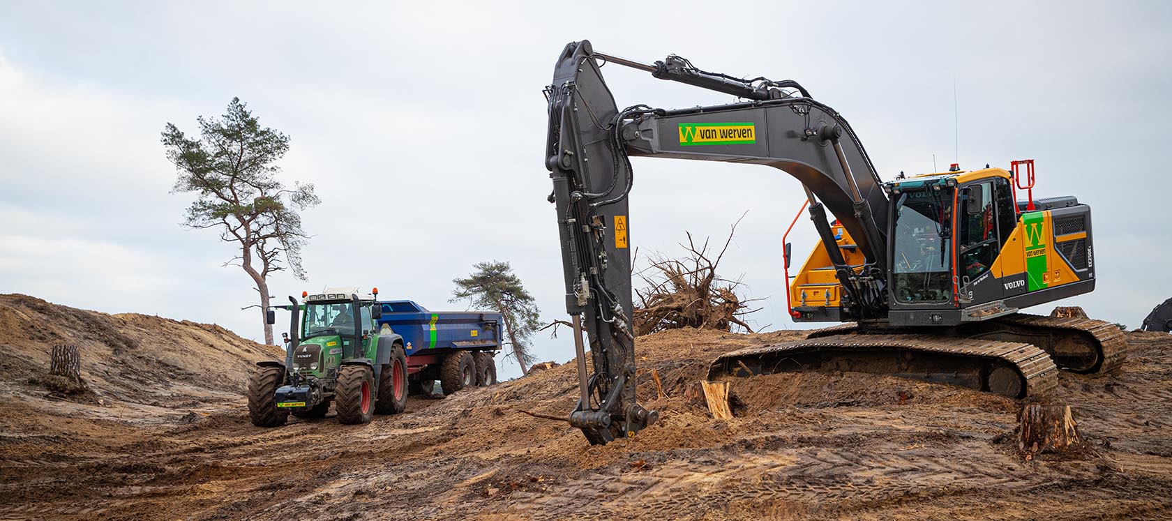 De Volvo-rupskraan aan het werk tussen de stronken, terwijl een Fendt-trekker met blauwe kipper voorbijrijdt
