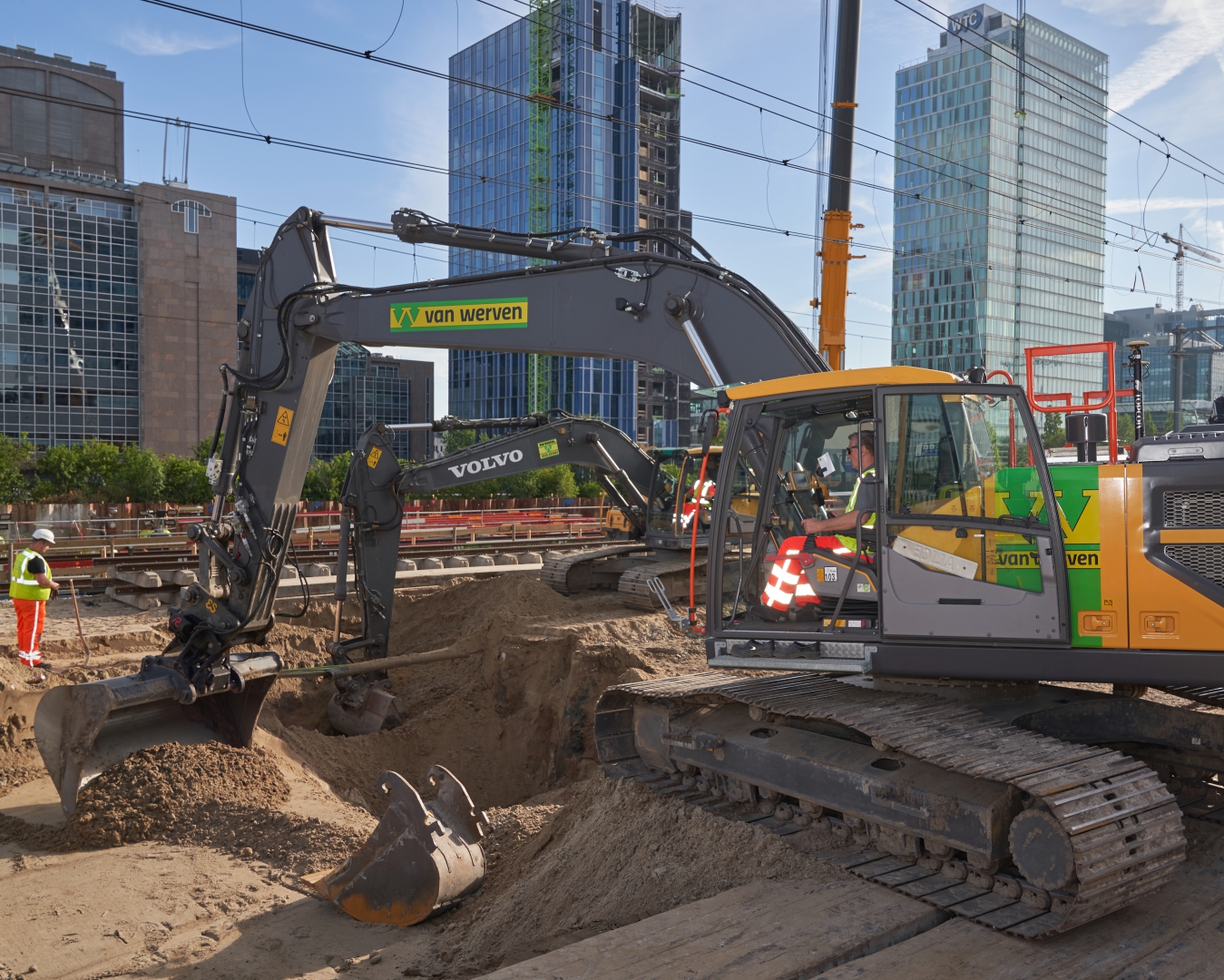 Rupskraan van Van Werven graaft langs het spoor op de Zuidas, met de kantoortorens erachter