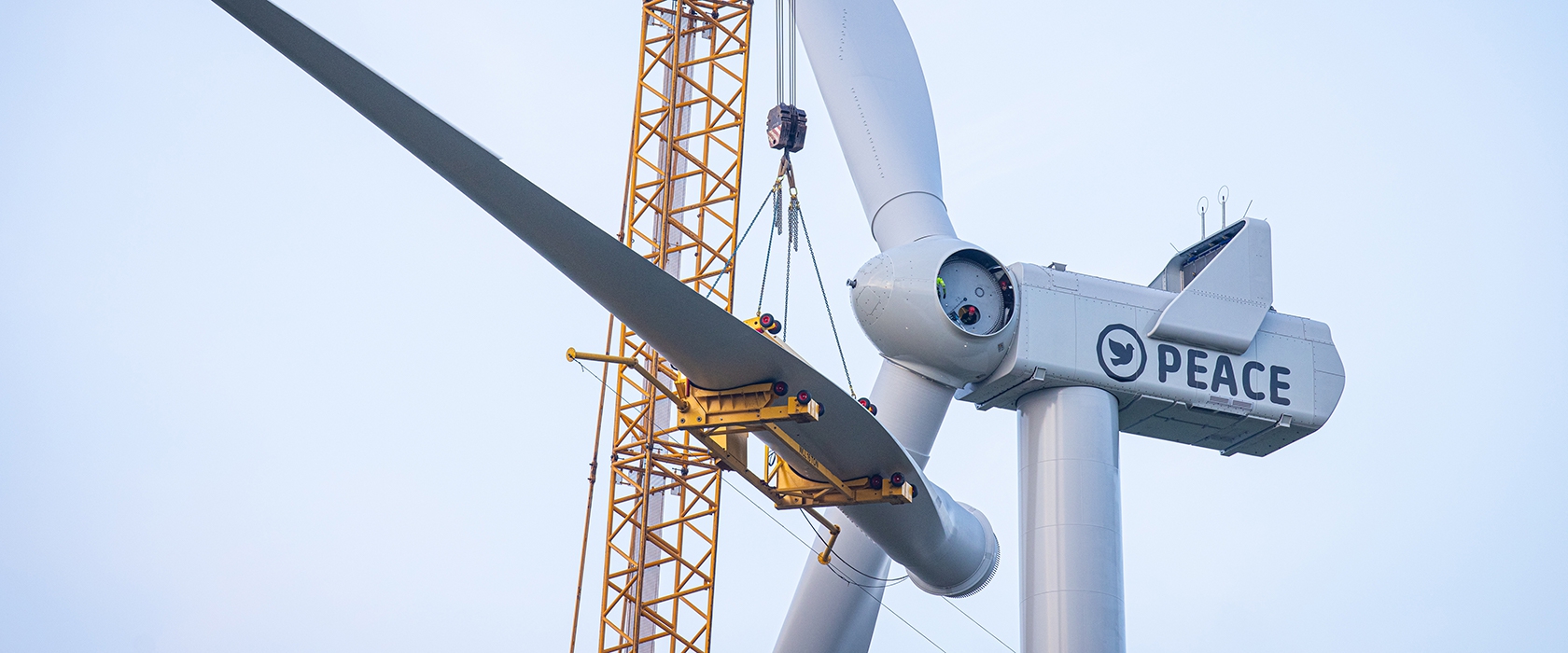 Een kraan hijst een rotorblad naar de gondel van de windmolen met de tekst 'Peace' en een vredesduif erop