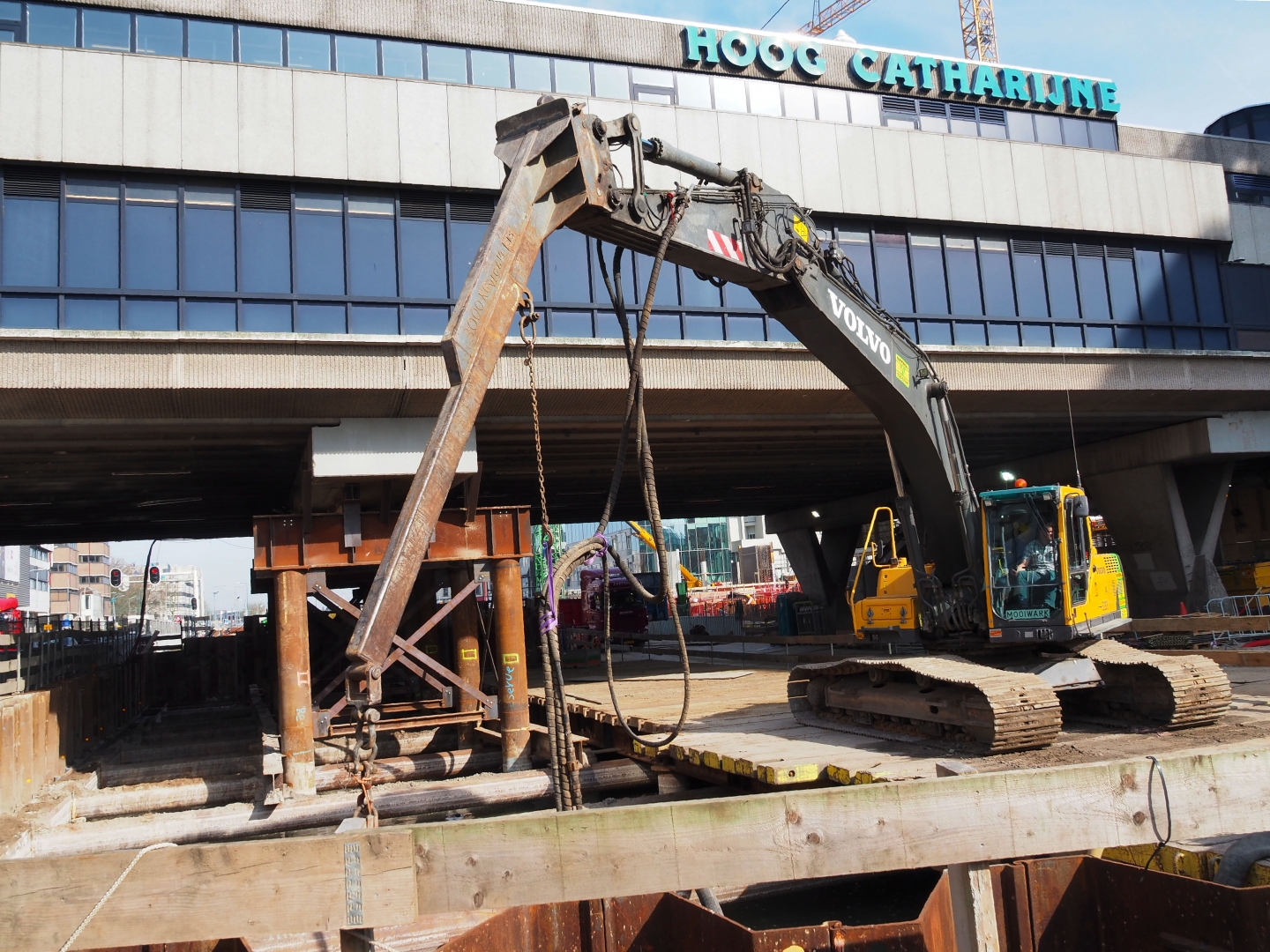 Een Volvo-rupskraan van Van Werven werkt vanaf het houten dek boven de bouwkuip, recht voor de letters van Hoog Catharijne