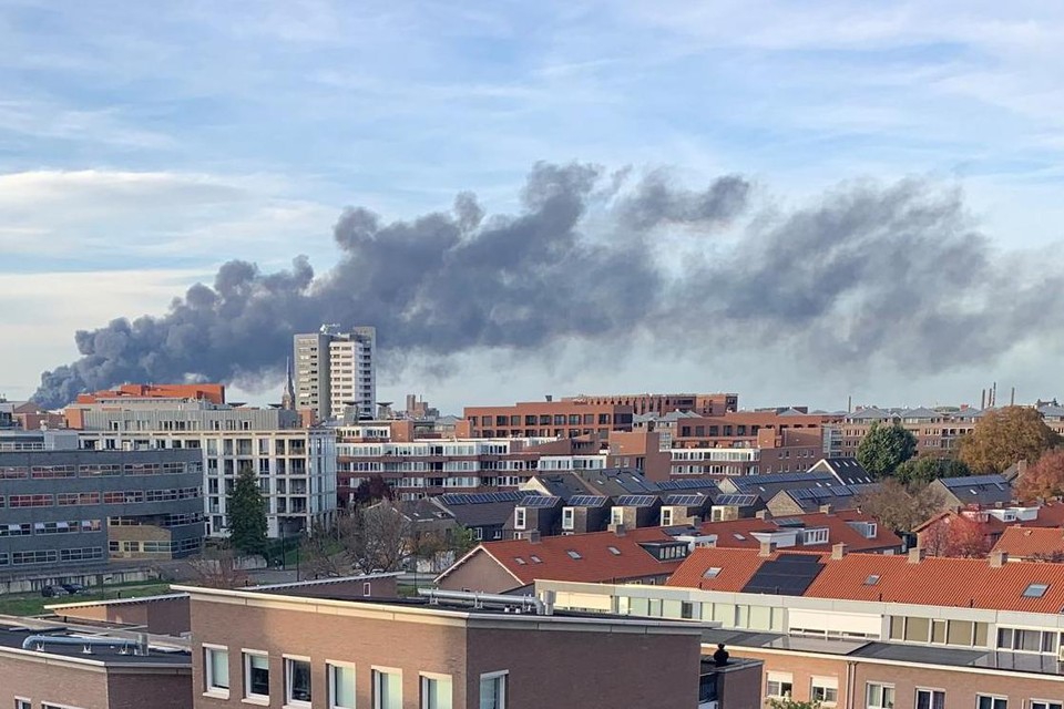 Grote donkere rookwolk boven de stad, gezien over de daken van woningen en flatgebouwen