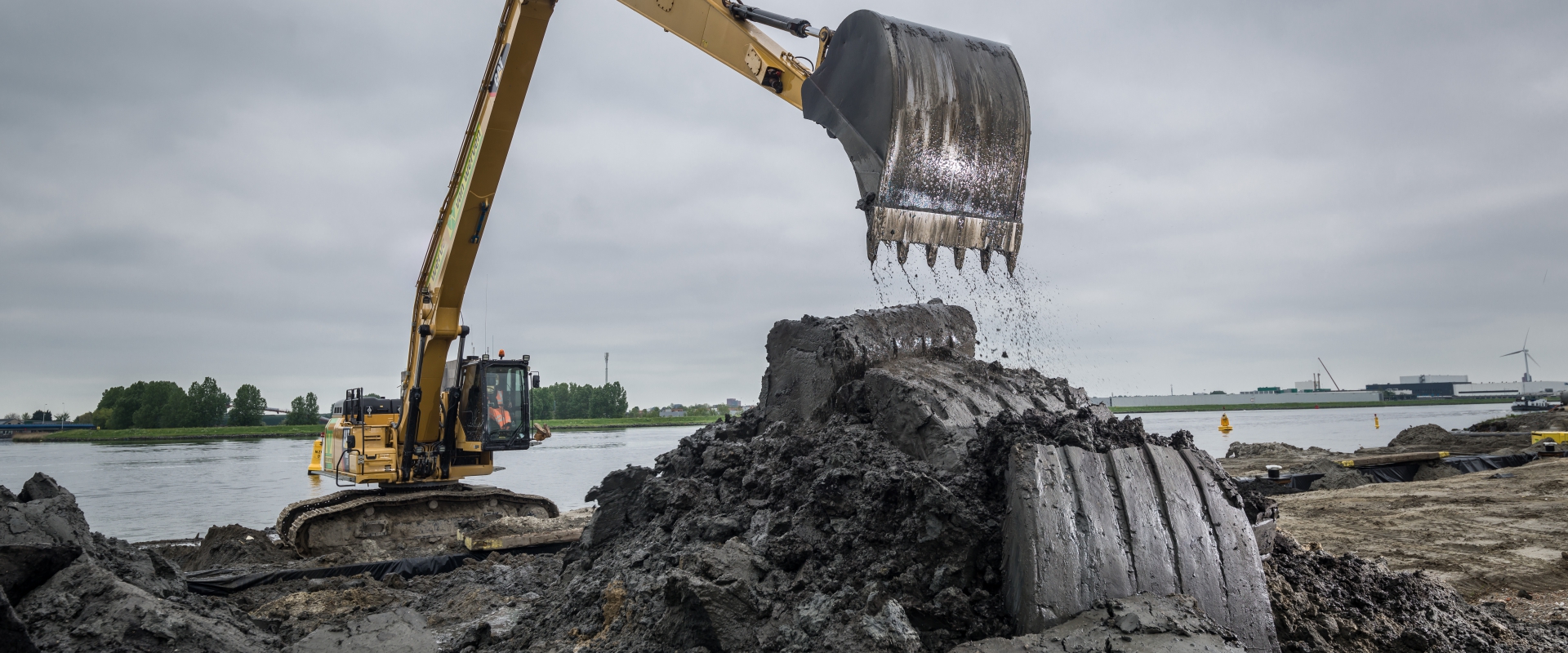 Rupskraan met lange giek schept natte klei aan de oever van een rivier