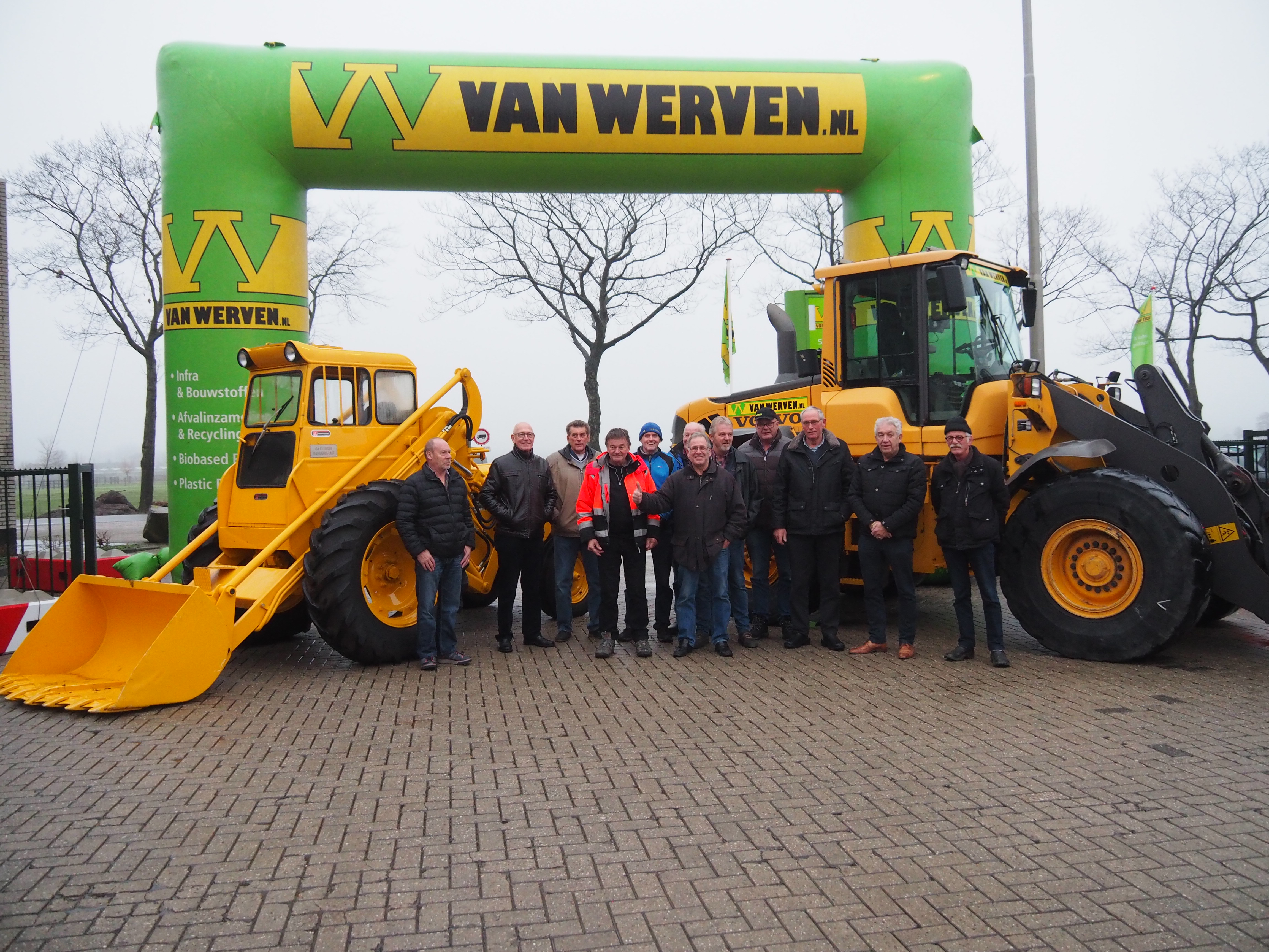 Collega’s poseren onder de Van Werven-boog bij de gerestaureerde oude shovel en een nieuwe Volvo