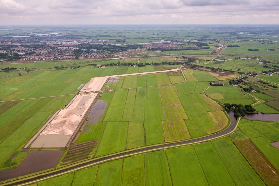 Luchtfoto van het polderlandschap bij Kampen, met een lange strook ontgraven zand door de weilanden en de stad aan de horizon