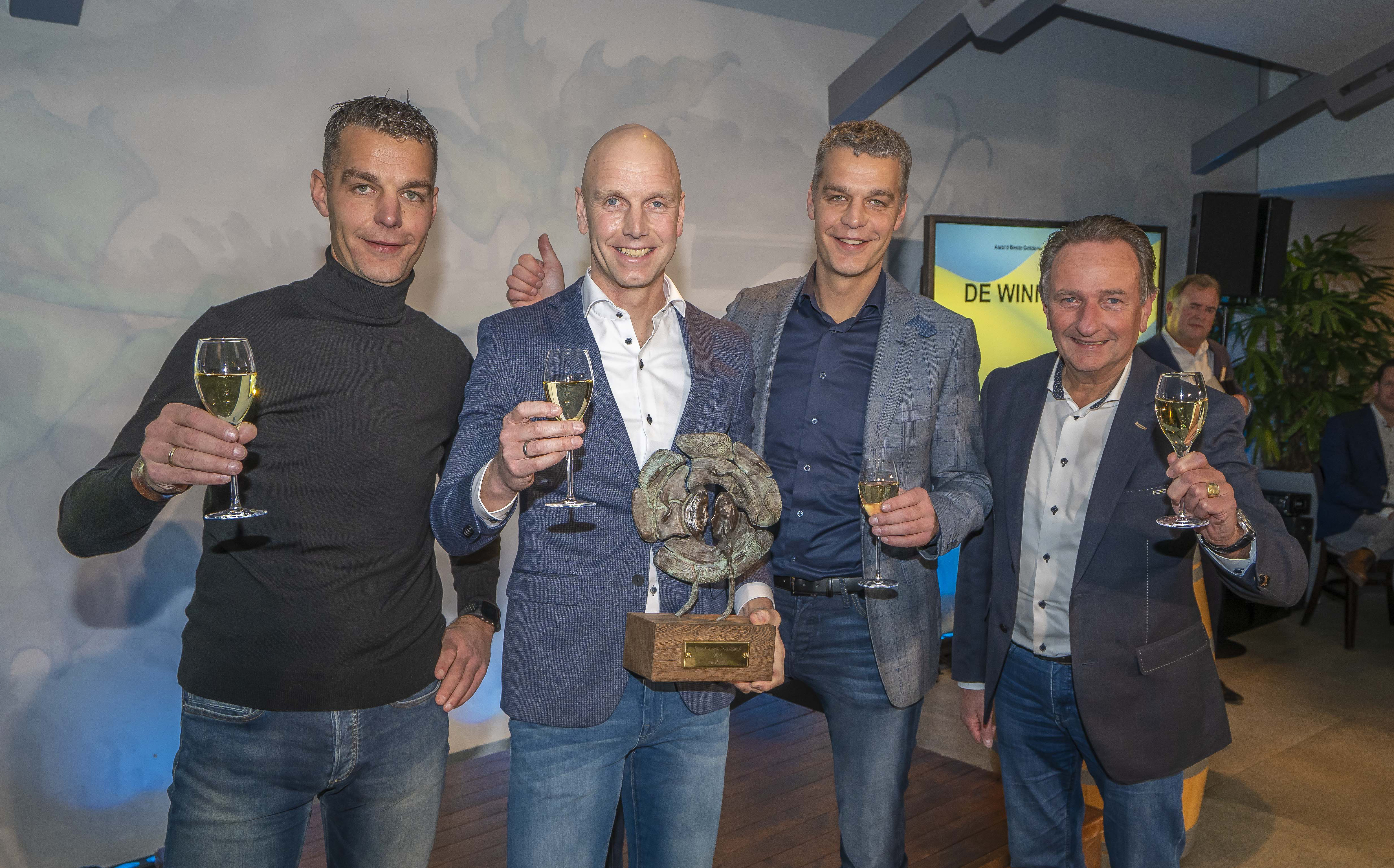 Vier mannen proosten met champagne rond het bronzen kunstwerk van de award