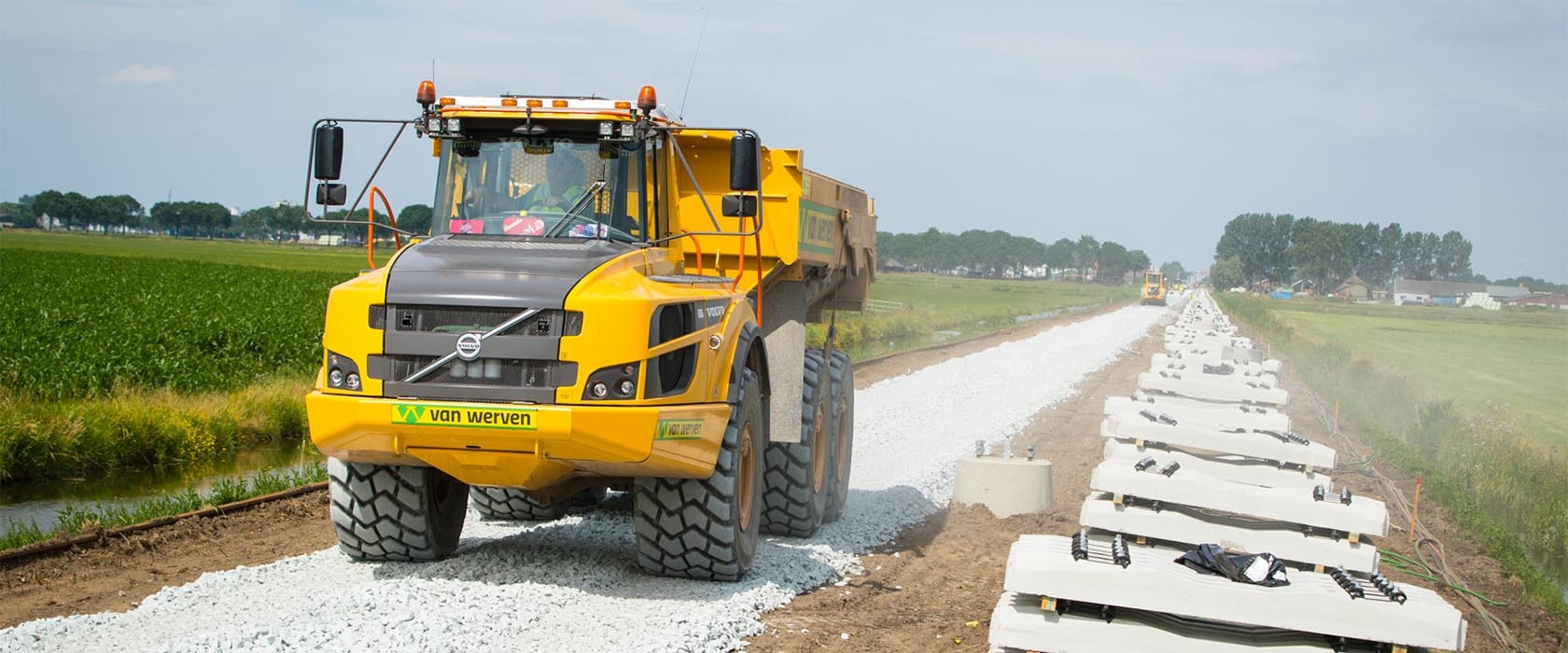 Een Volvo-dumper van Van Werven rijdt over het nieuwe ballastbed, met pakketten dwarsliggers klaar langs het spoor