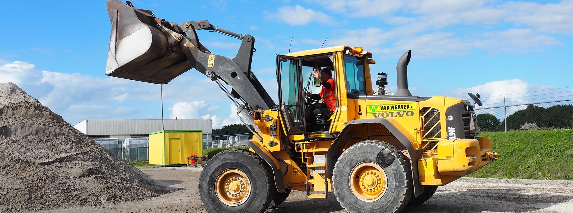 Machinist zwaait vanuit de cabine van zijn Volvo-shovel bij een zandberg