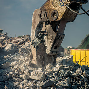 Sloopschaar die een brok beton vastheeft boven een berg puin