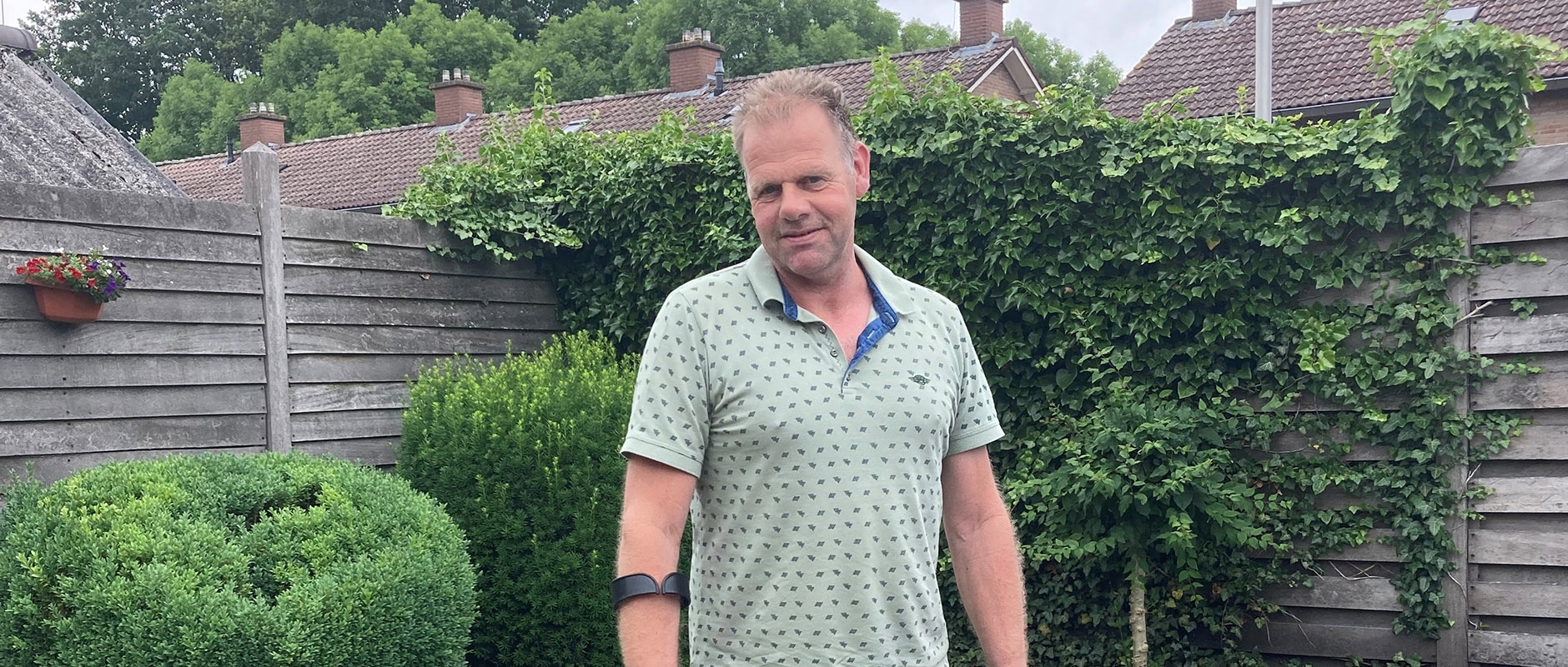 Henk staat in zijn achtertuin, met de elleboogkruk om zijn rechterarm