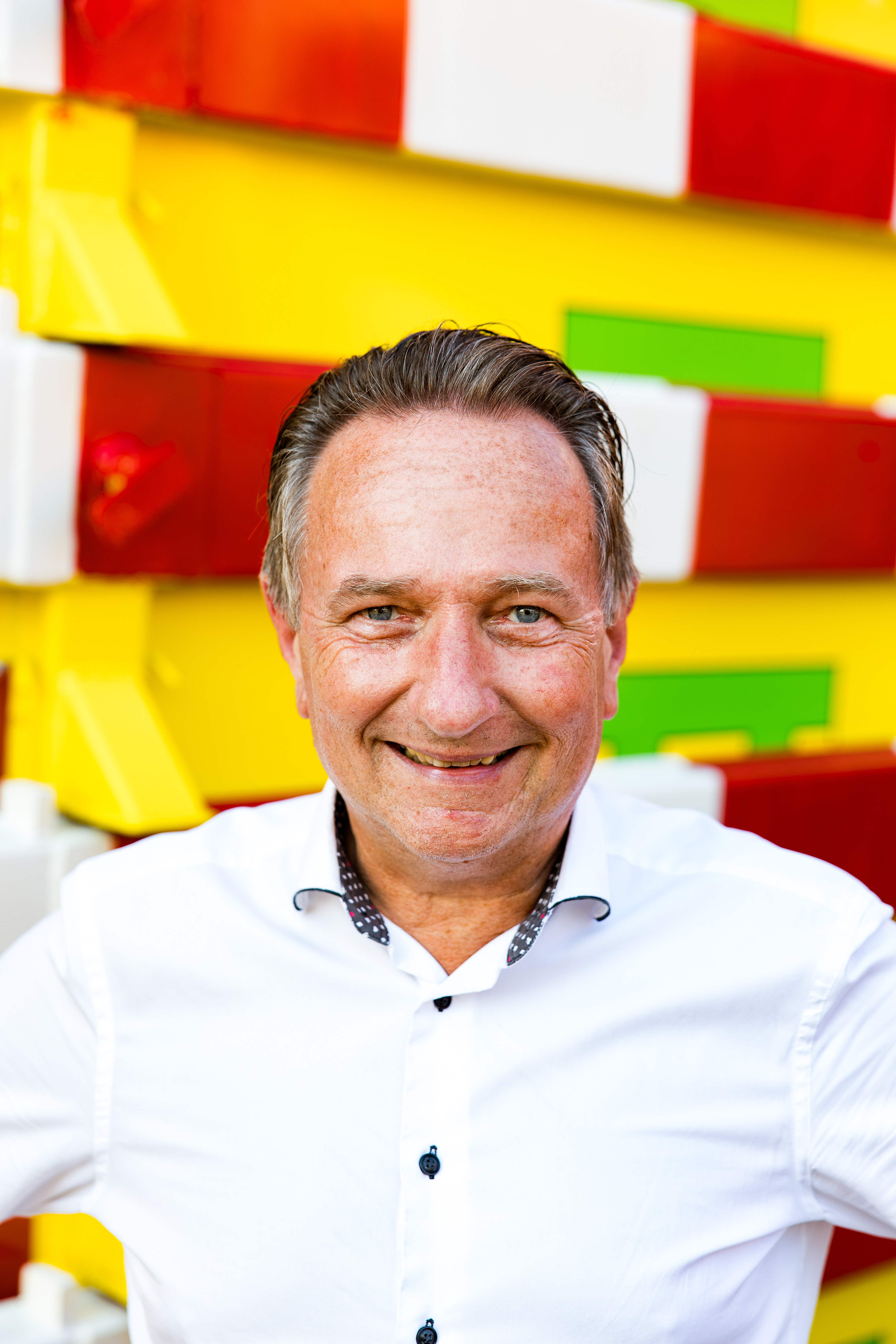 Portret van een lachende man in wit overhemd voor gestapelde geel-rode containers