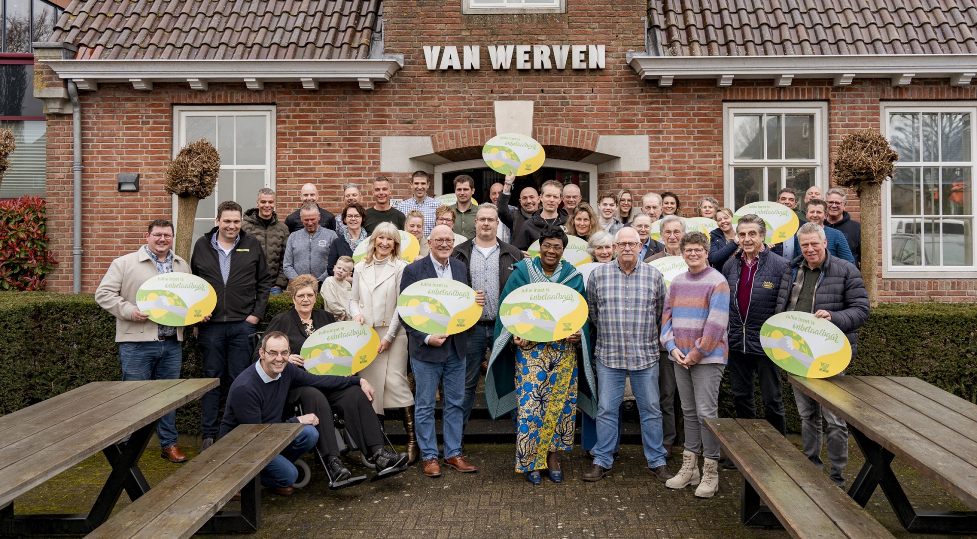 Groepsfoto van vertegenwoordigers van zeventien goede doelen met ronde borden 'Jullie inzet is onbetaalbaar' voor het Van Werven-kantoor