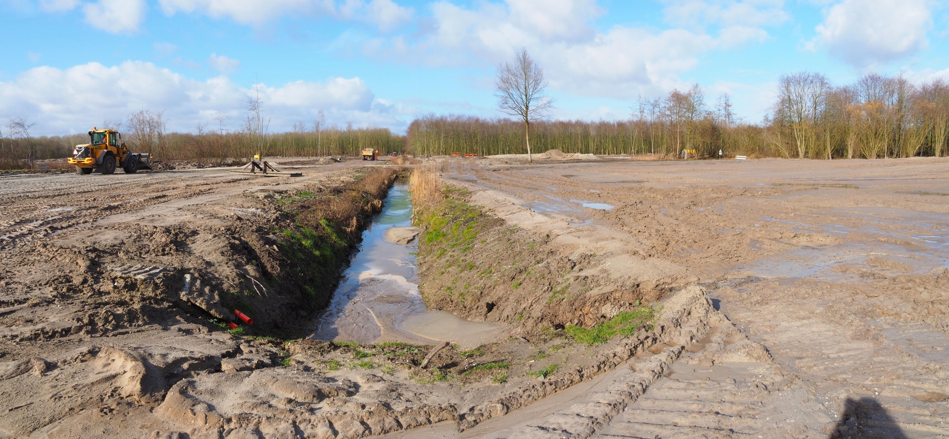 Het natte werkterrein op het scoutinglandgoed: een Volvo-wiellader bij de watervoerende sloot, langs de bosrand