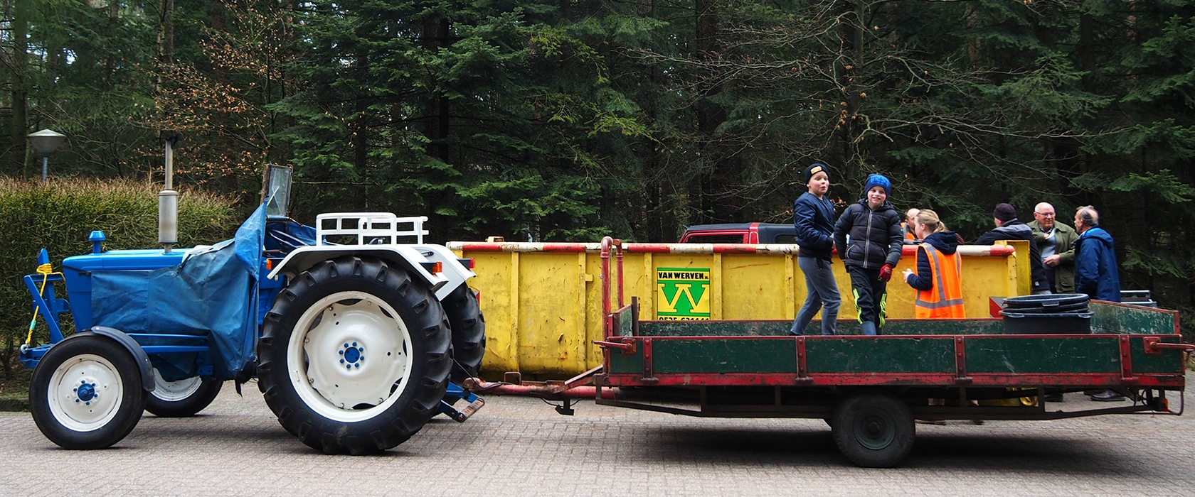 Kinderen op de aanhanger achter de oude Ford-tractor met een Van Werven-container tijdens de opschoonactie