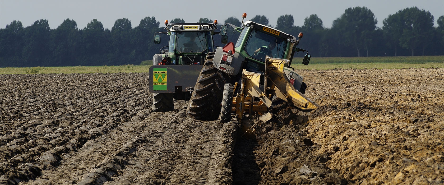 Twee trekkers van Van Werven diepploegen een akker; de ploeg keert de grondlagen