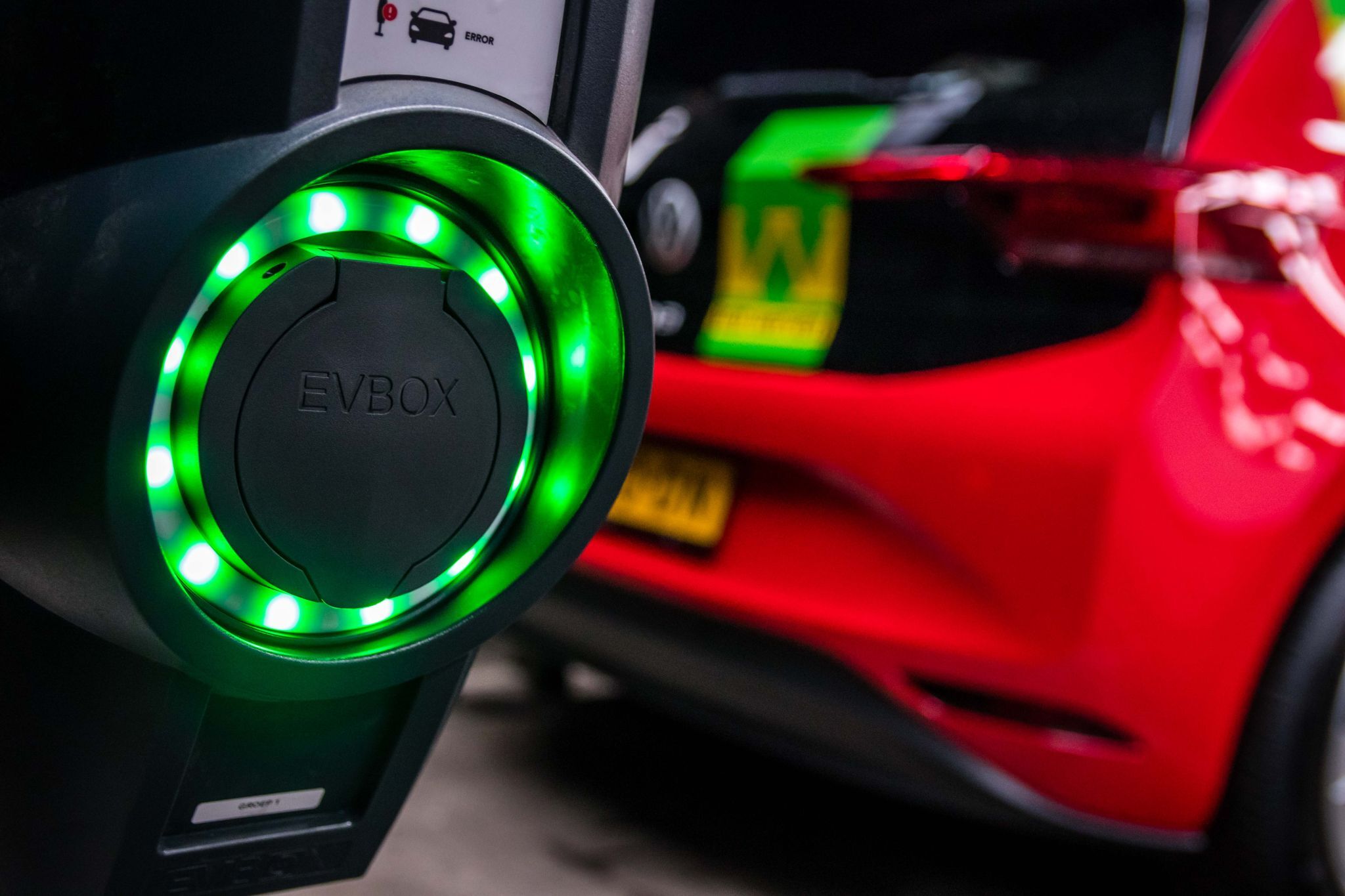 Close-up van een EVBox-laadpunt met groene ledring; op de achtergrond een rode ID.3 met Van Werven-logo