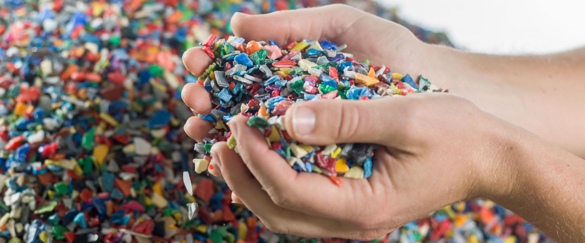 Handen vol kunststof maalgoed boven een berg gekleurde flakes