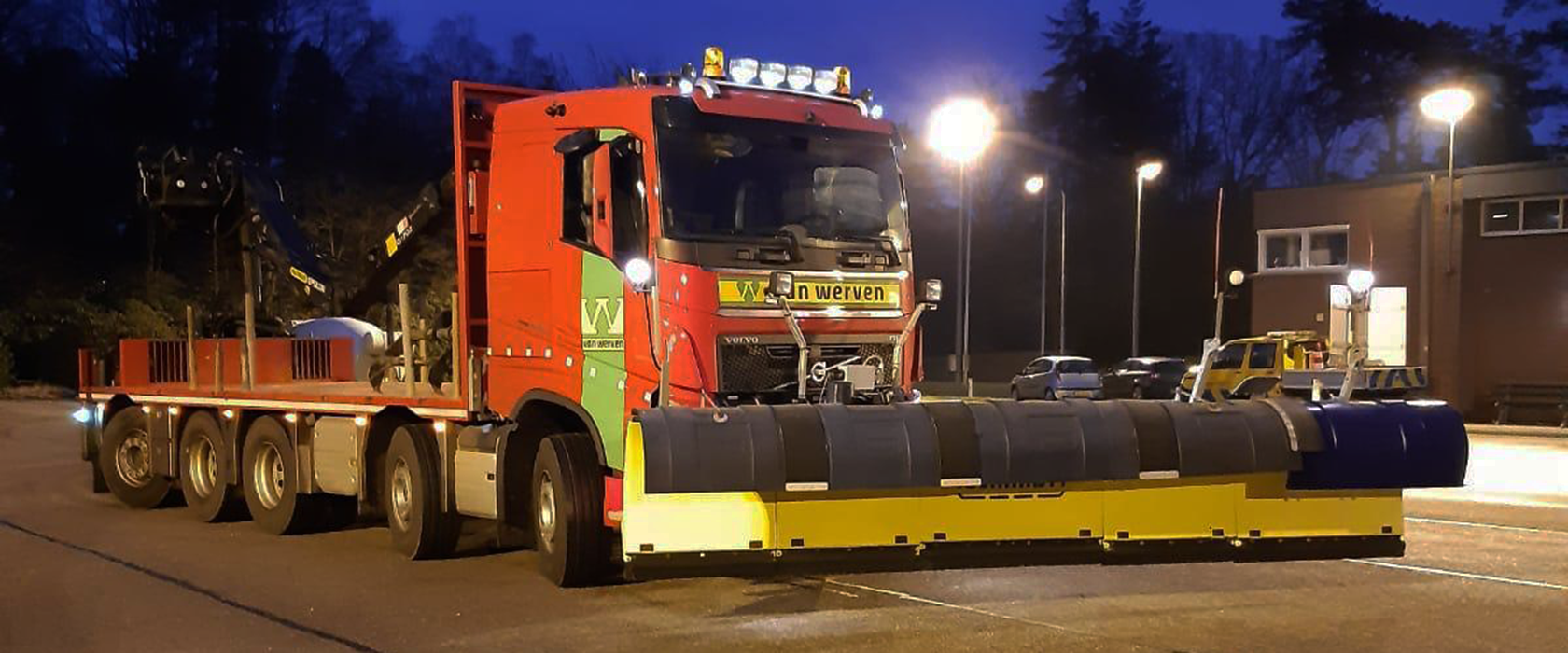 Vrachtwagen van Van Werven met brede strooi-installatie staat 's avonds op een verlicht parkeerterrein