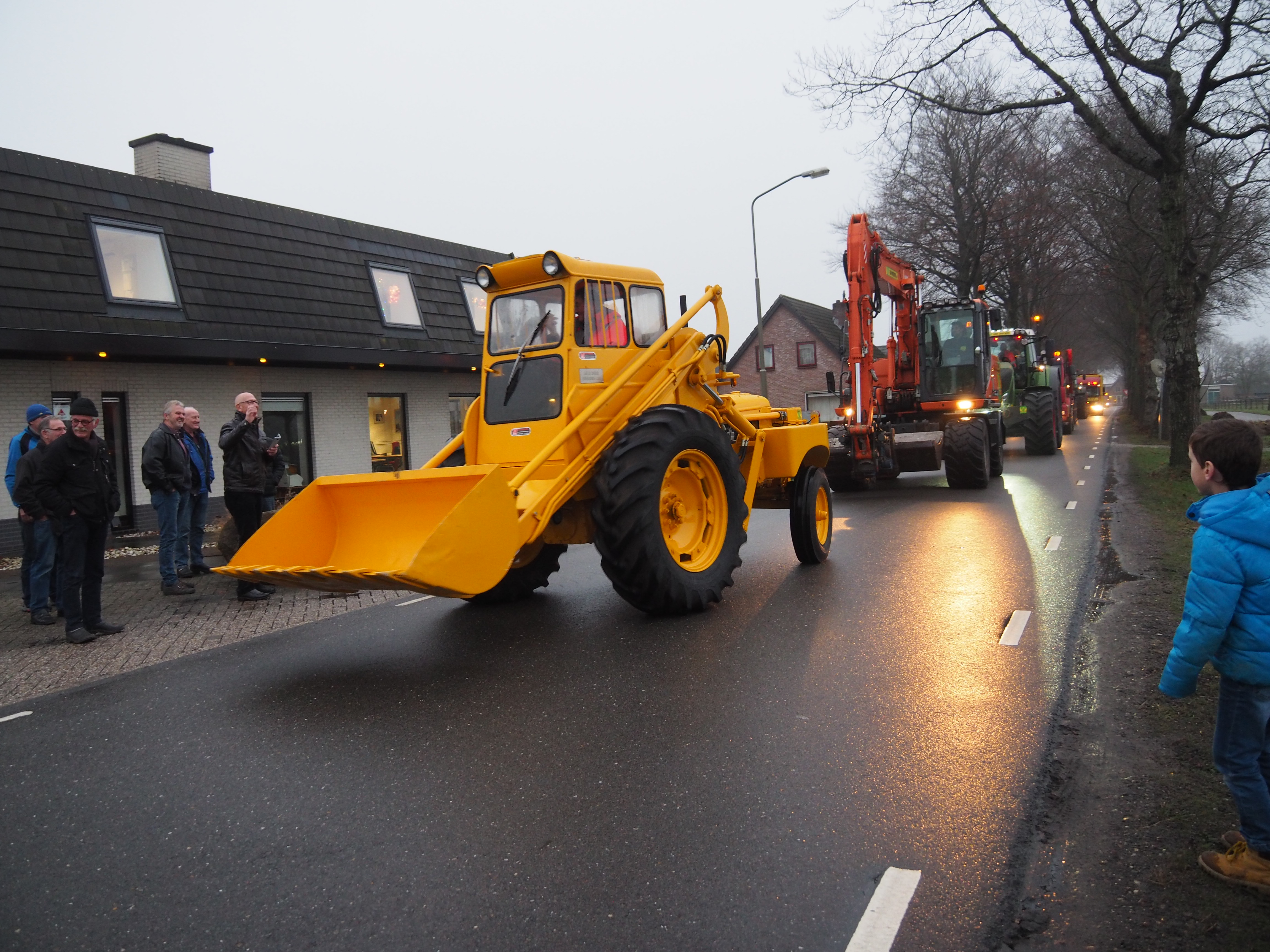 De gerestaureerde gele shovel rijdt voorop in een stoet machines door het dorp