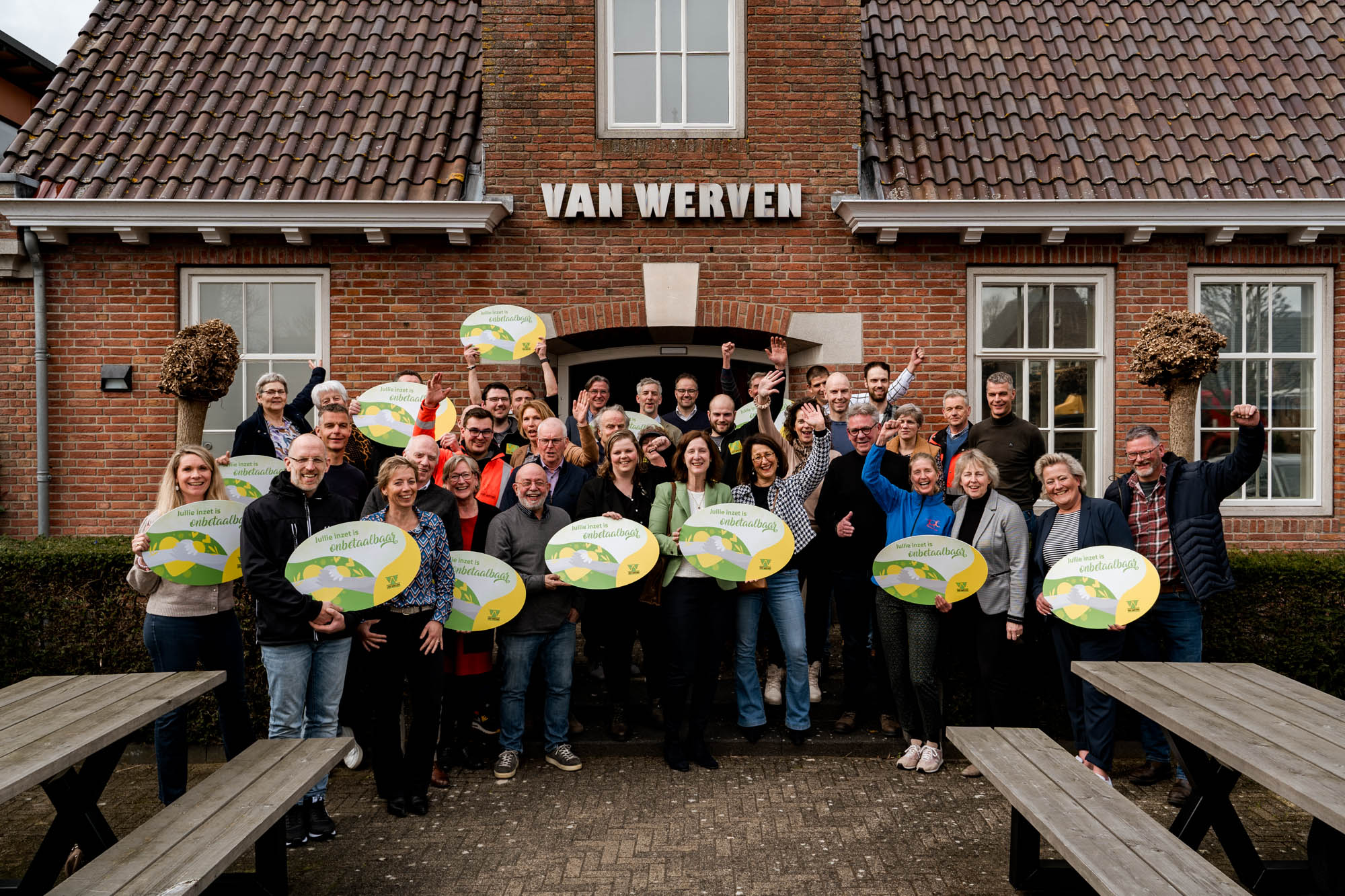 Juichende groepsfoto van de vertegenwoordigers met de ronde borden 'Jullie inzet is onbetaalbaar' voor het Van Werven-kantoor