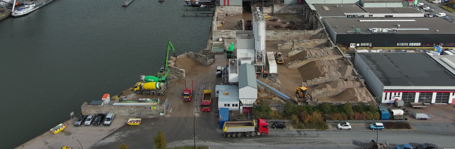 Panoramische luchtfoto van het terrein in Harderwijk aan het water, met betonmixers, zandvakken en het weegkantoor