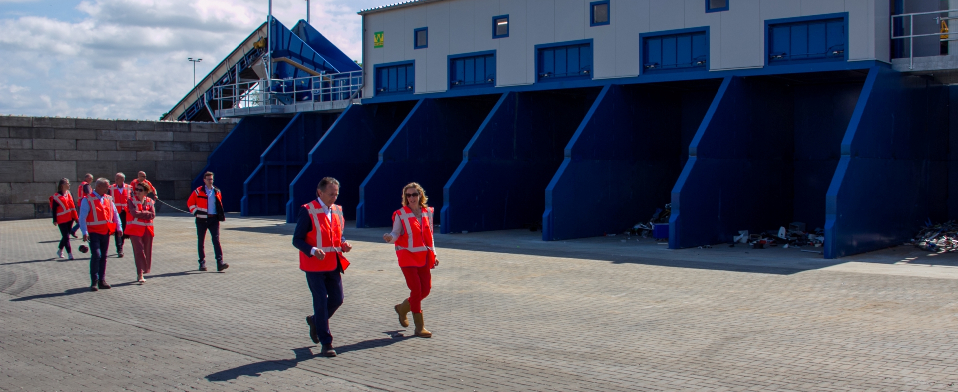 Gezelschap in oranje veiligheidshesjes loopt over het terrein langs de nieuwe blauwe sorteerinstallatie