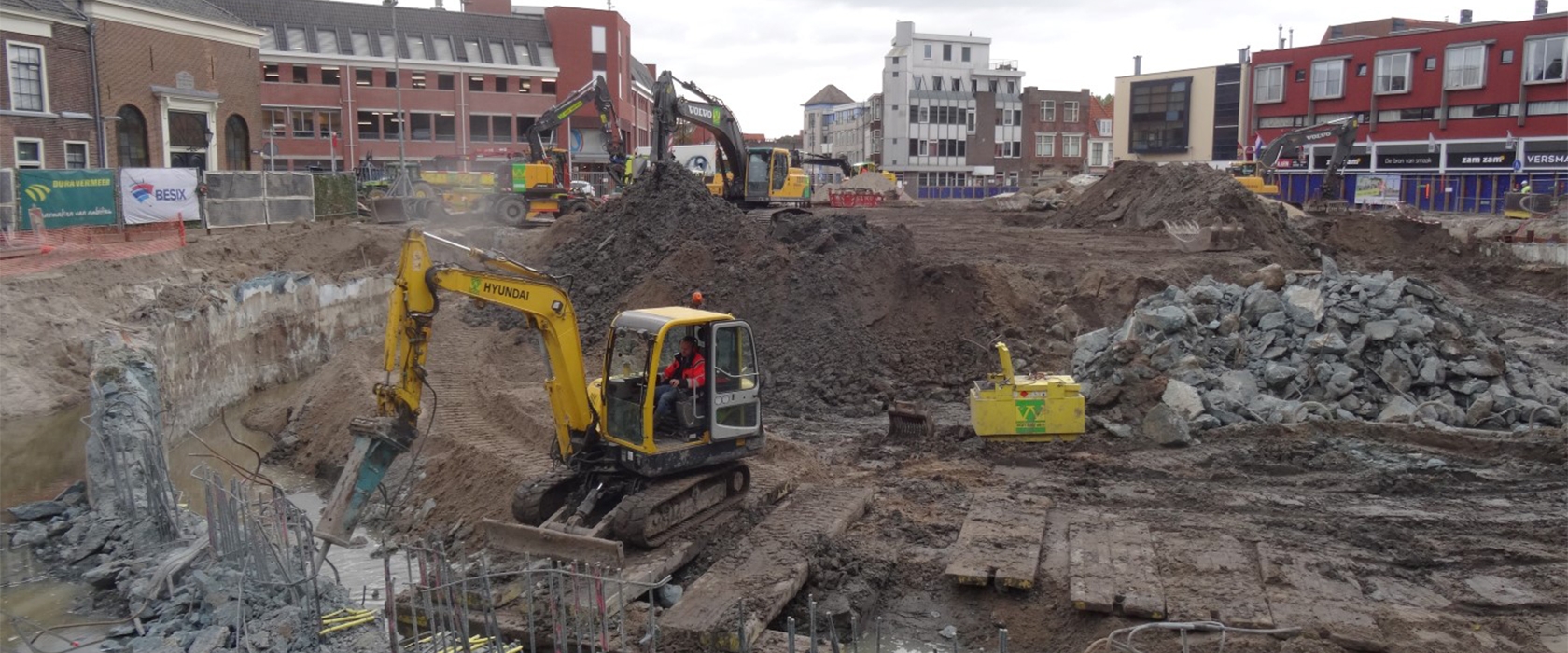 Een minigraver met sloophamer breekt puin in de diepe ontgraving, terwijl kranen van Van Werven op de grondbergen werken