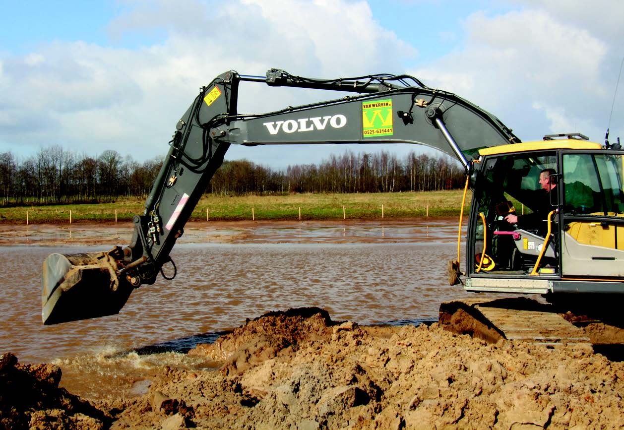 De Volvo-kraan van dichtbij: de machinist kijkt vanuit de cabine naar de bak die vlak boven het water hangt