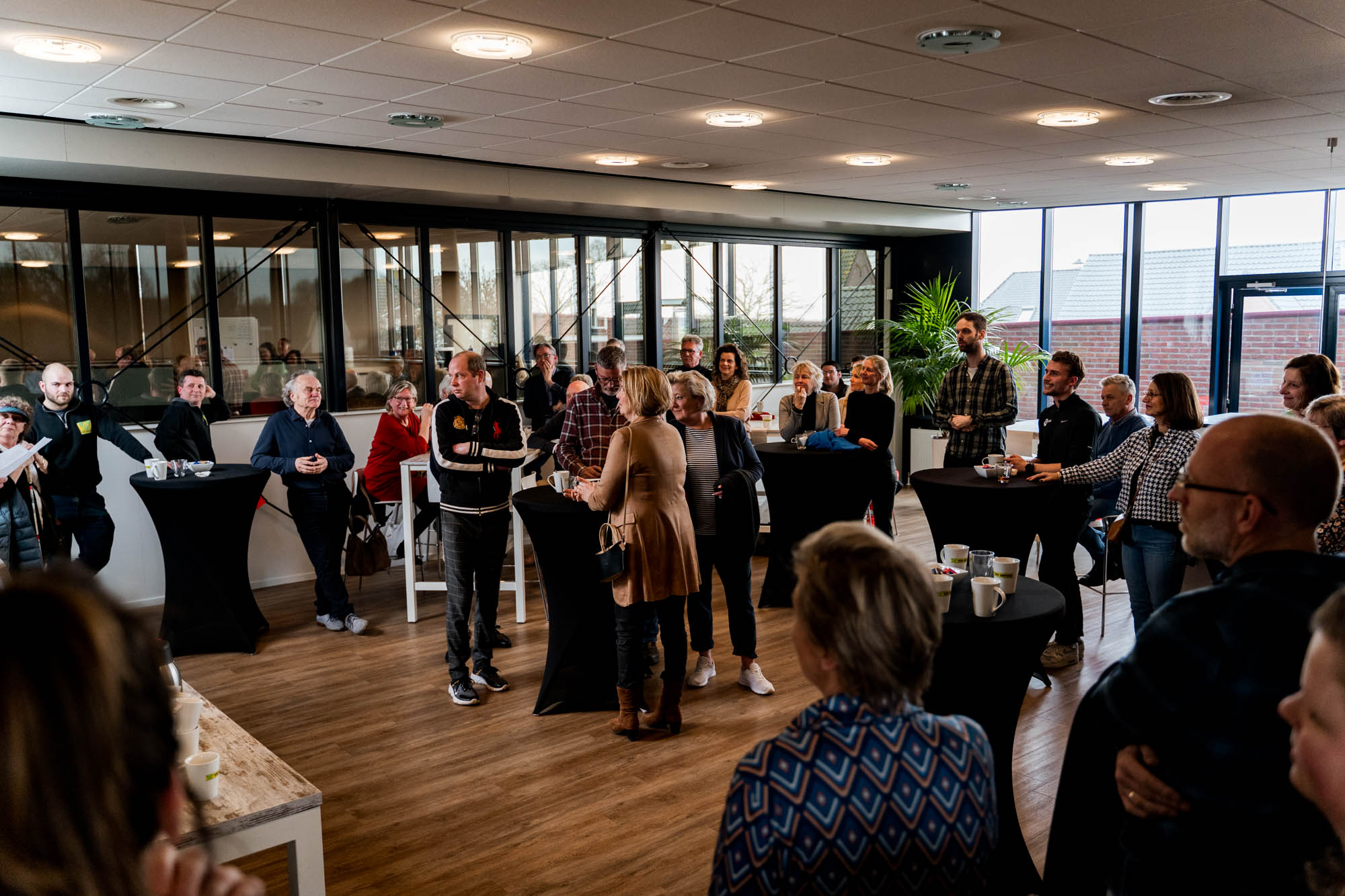 Genodigden van de goede doelen staan rond zwarte statafels met koffie in de ontvangstruimte