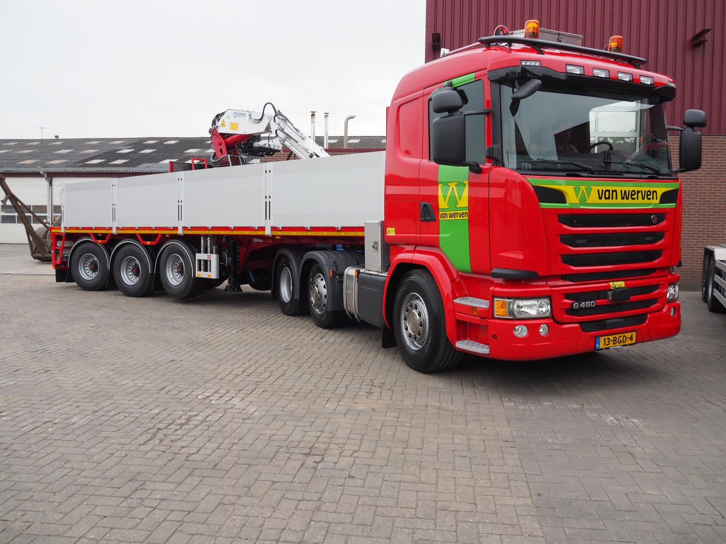 De vrachtwagen met rijplatentrailer en autolaadkraan, gezien vanaf de cabinezijde