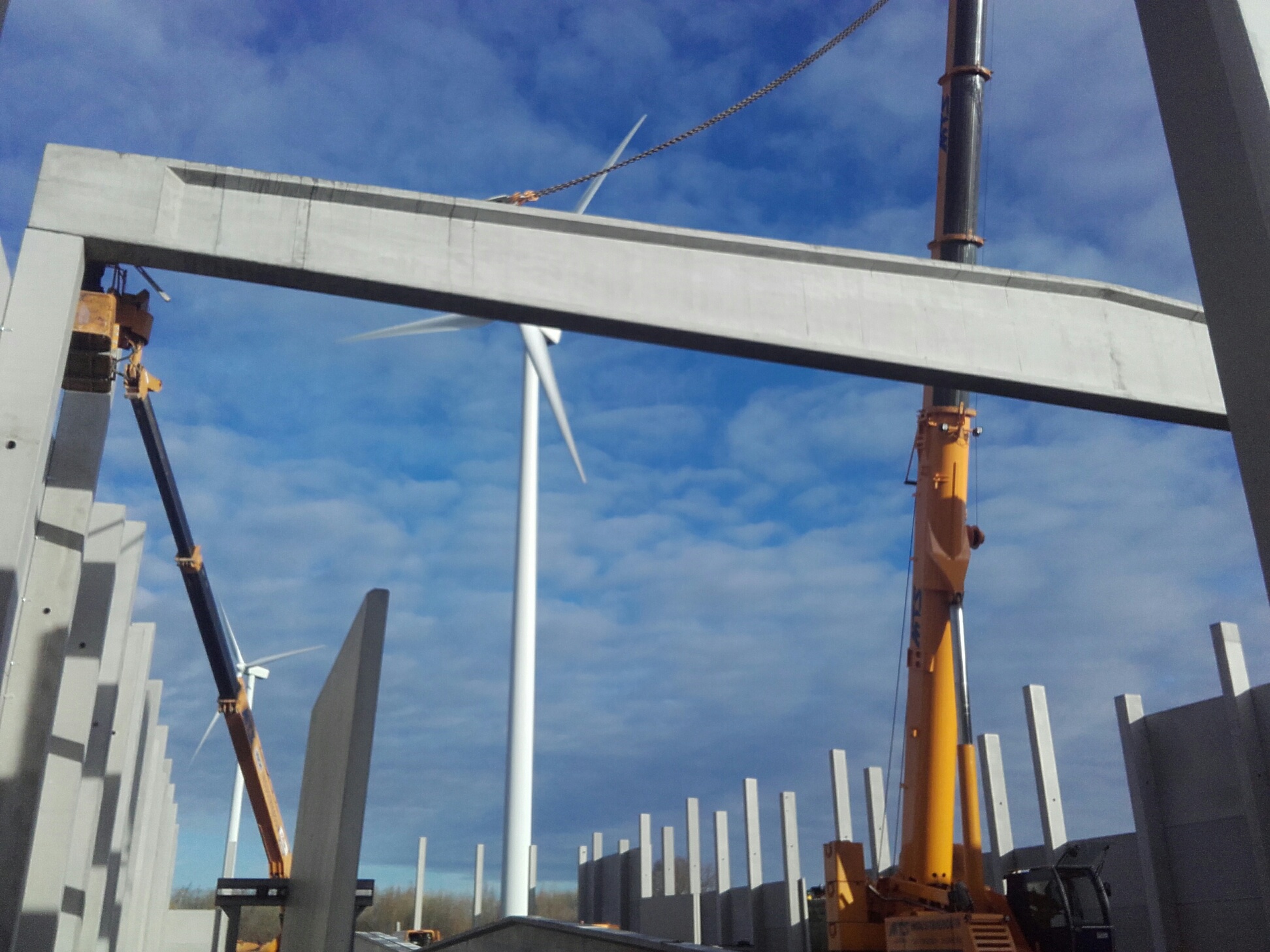 Telekraan hijst een betonnen balk op zijn plek, met windmolens op de achtergrond