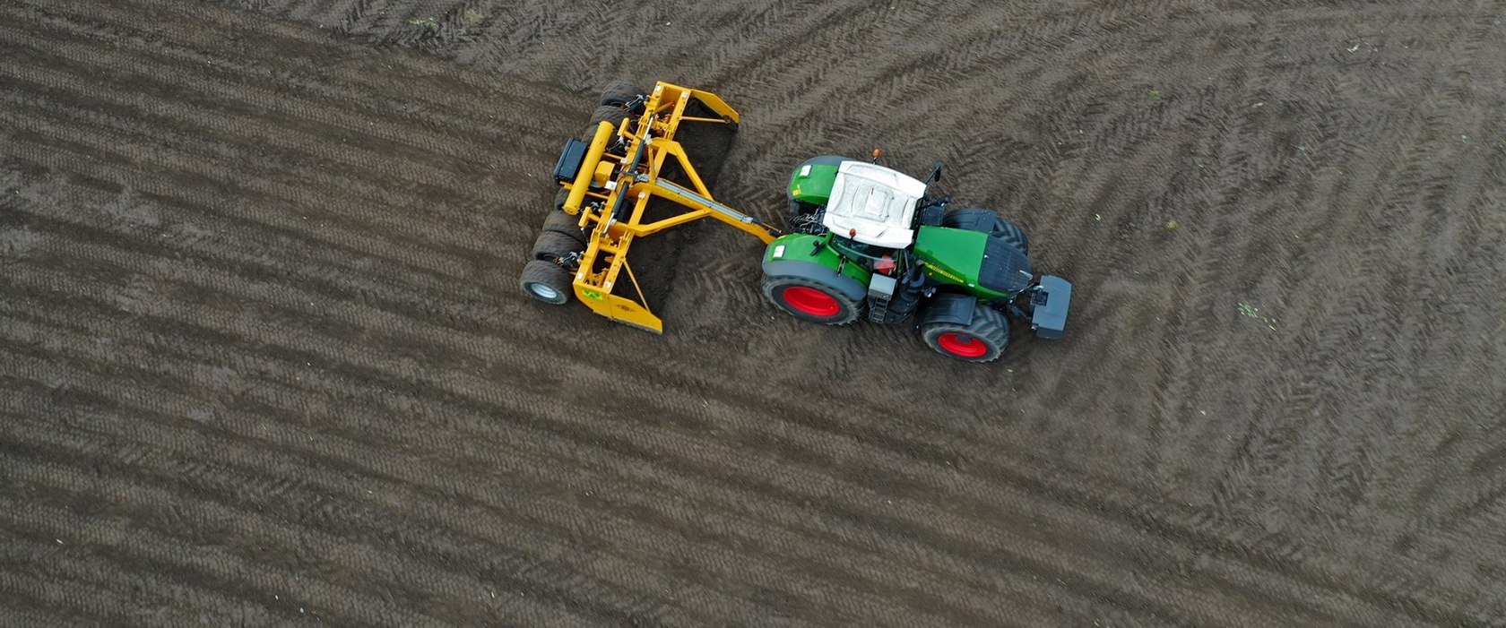 Dronefoto van een groene Fendt-trekker van Van Werven met gele kilverbak op een donkere, vlakgetrokken kavel