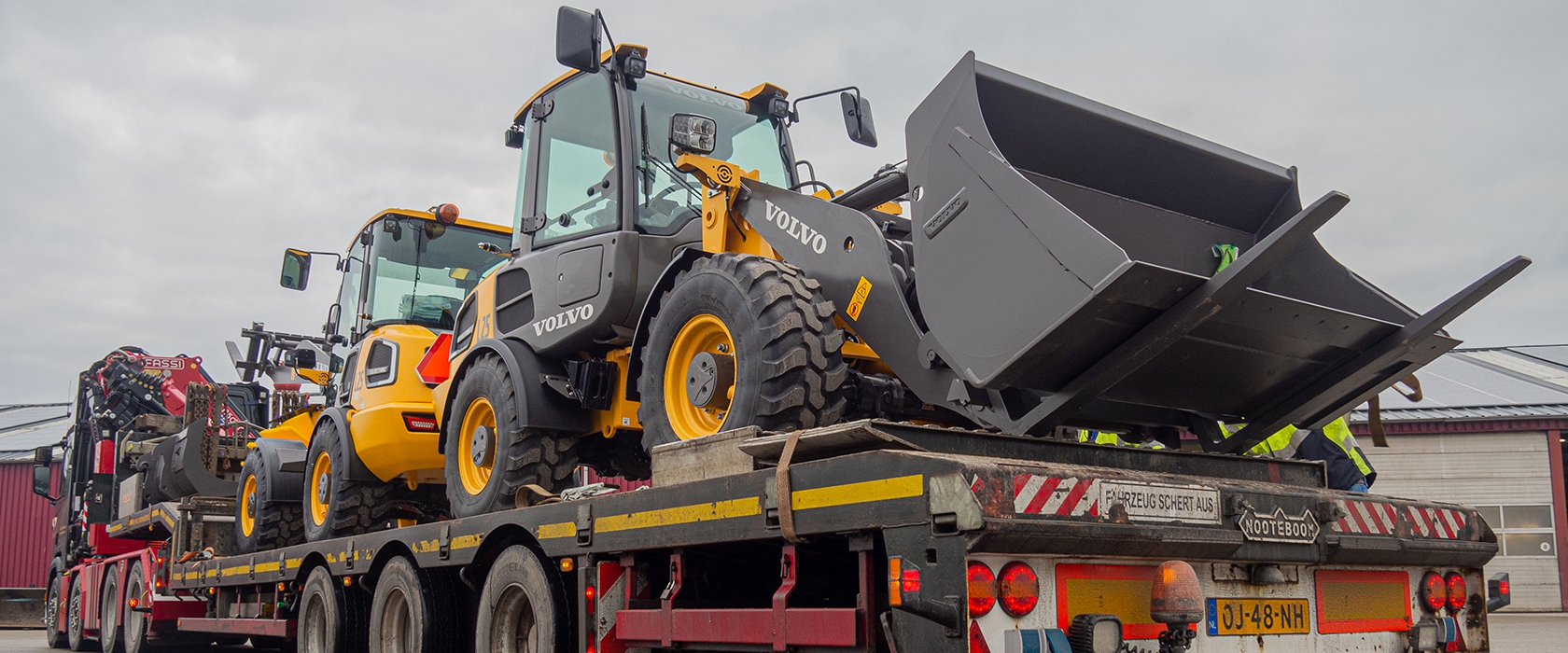 Twee nieuwe Volvo wielladers staan vastgezet op een dieplader bij aflevering