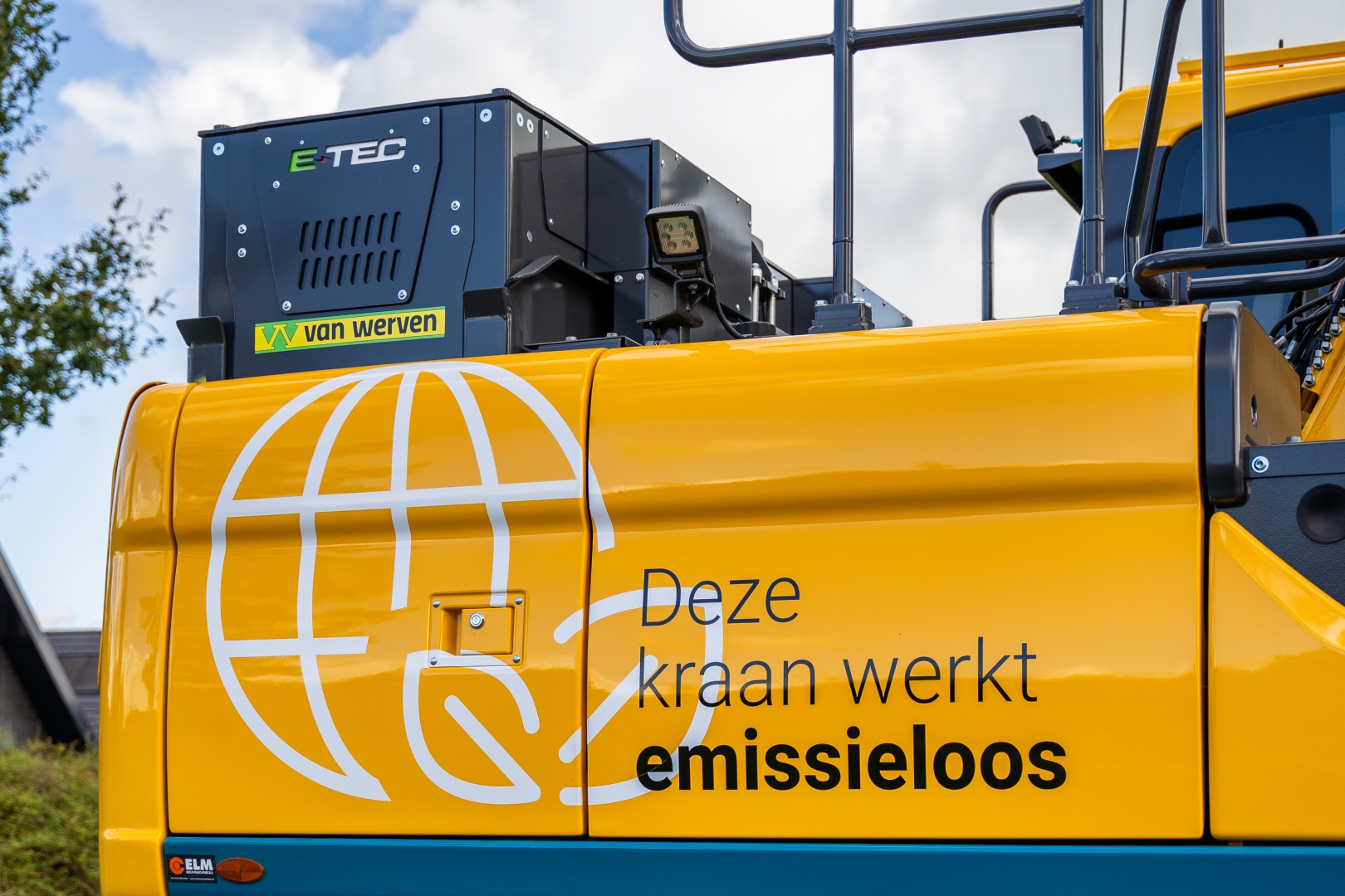 Close-up van de gele elektrische kraan met de tekst 'Deze kraan werkt emissieloos' en een E-TEC-accupakket met Van Werven-logo bovenop