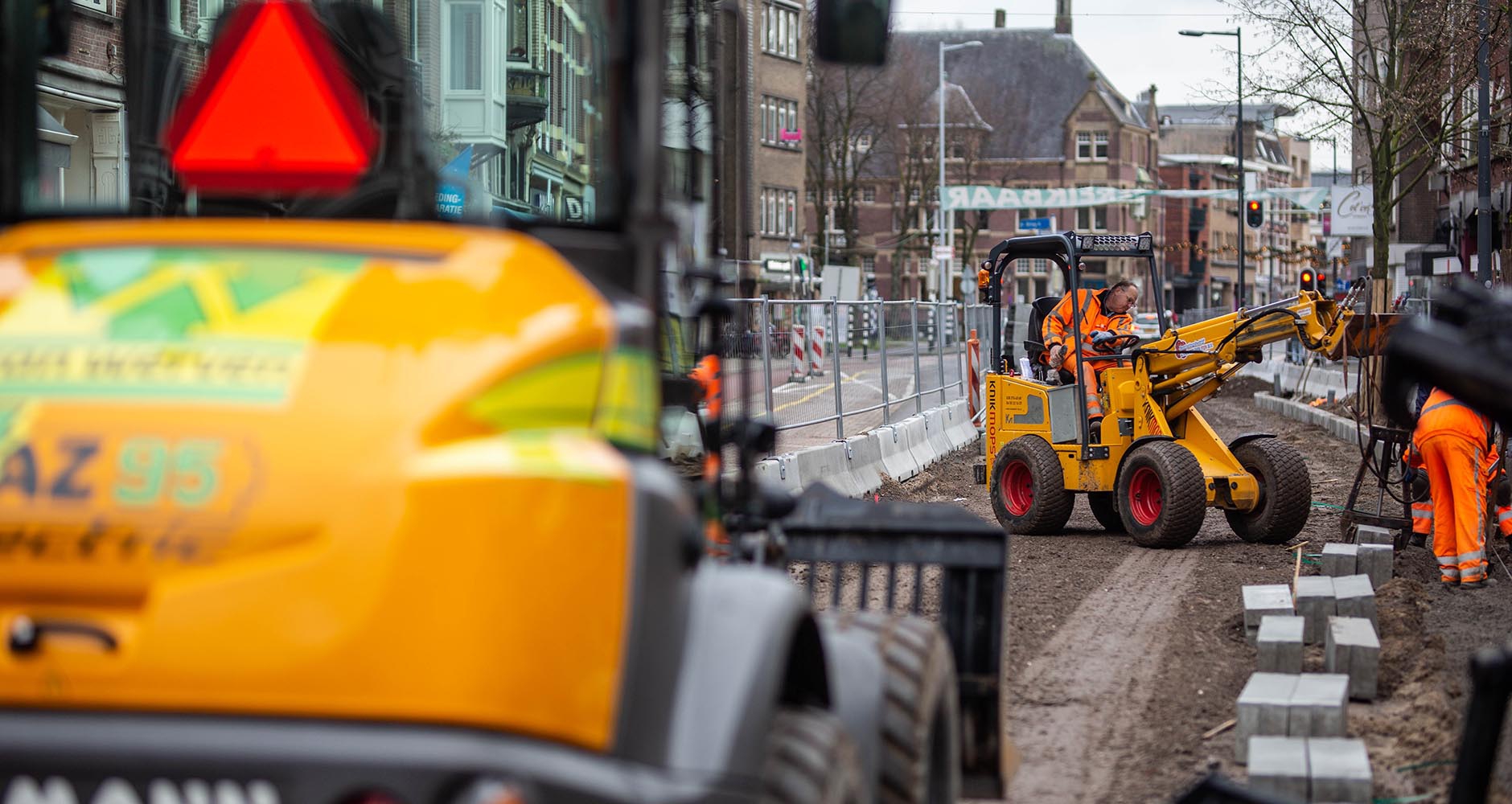 Werk in de Utrechtse winkelstraat: een elektrische knikmops zet stoepbanden, met de elektrische shovel van Van Werven op de voorgrond