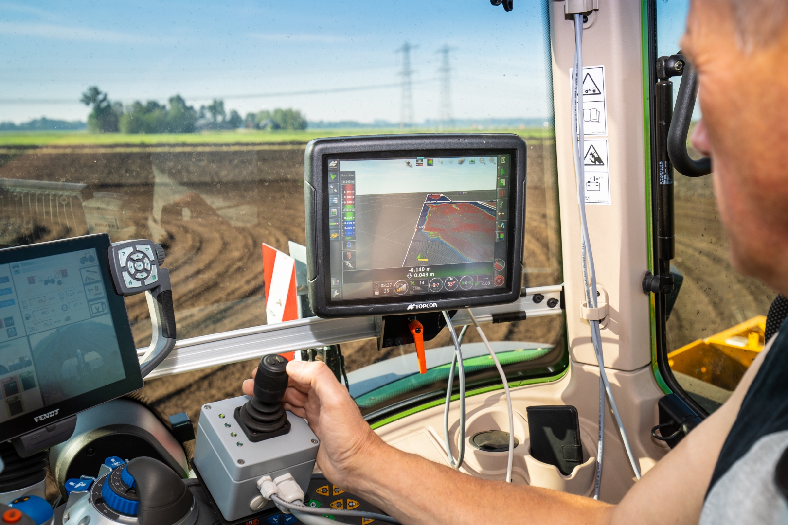 Het scherm in de cabine toont het 3D-model van de kavel, met de hand van de machinist op de joystick ernaast