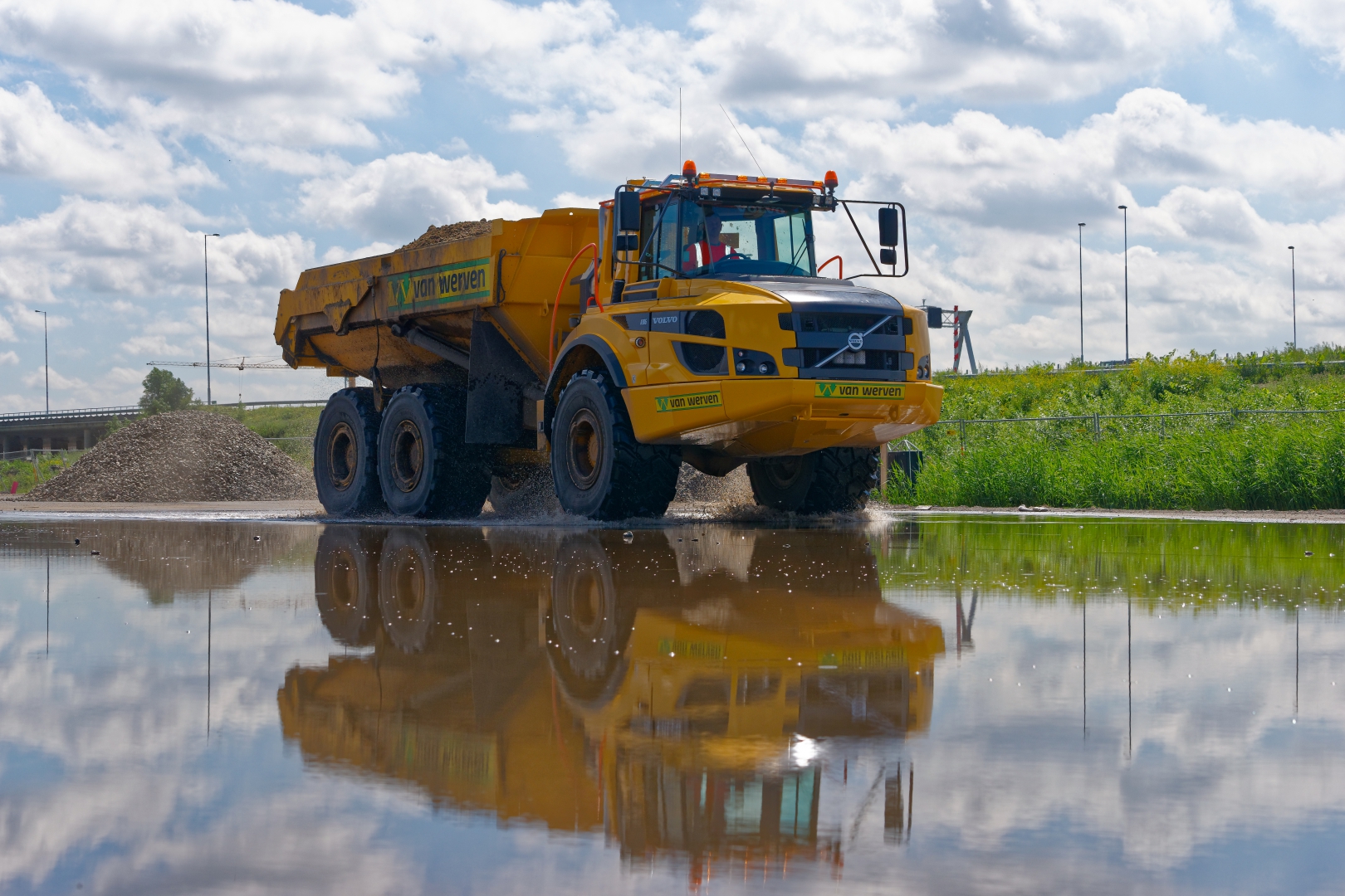 Gele Volvo-knikdumper van Van Werven rijdt door een plas op het werkterrein