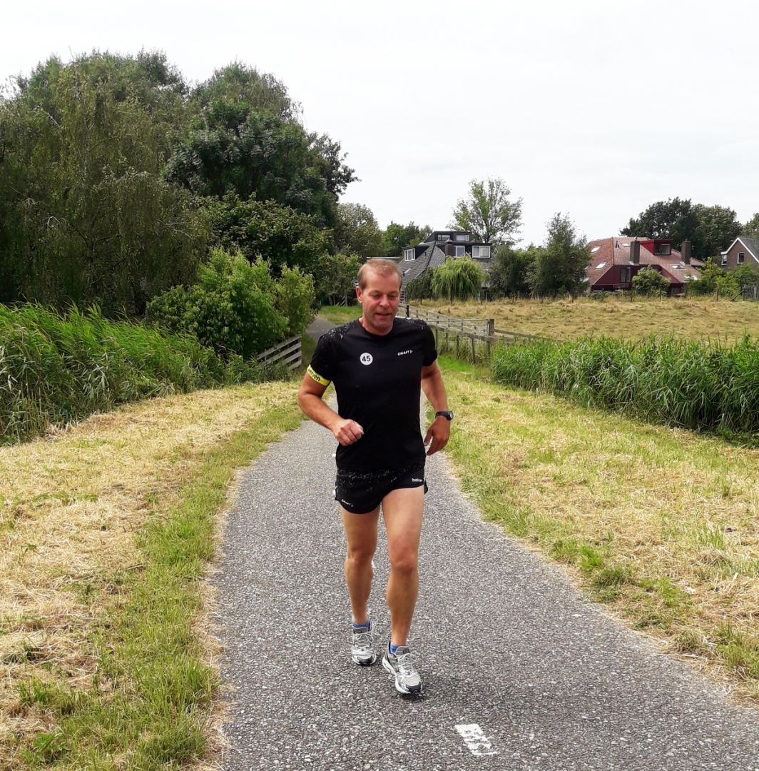 De hardloper in het zwarte runningshirt komt met startnummer 45 over het fietspad tussen de weilanden aangelopen