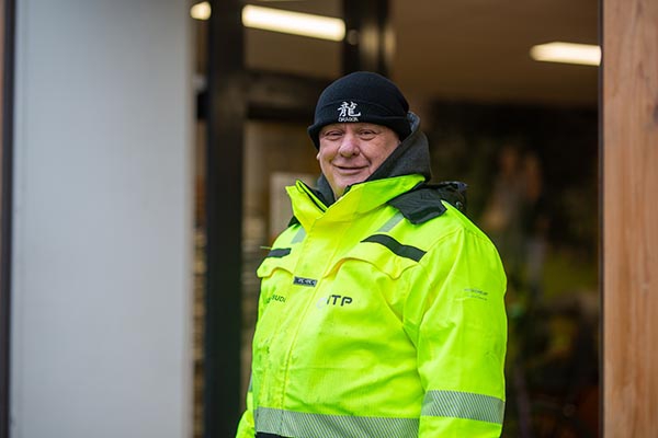 Portret van een medewerker van NTP in gele werkjas en zwarte muts voor de winkelpui