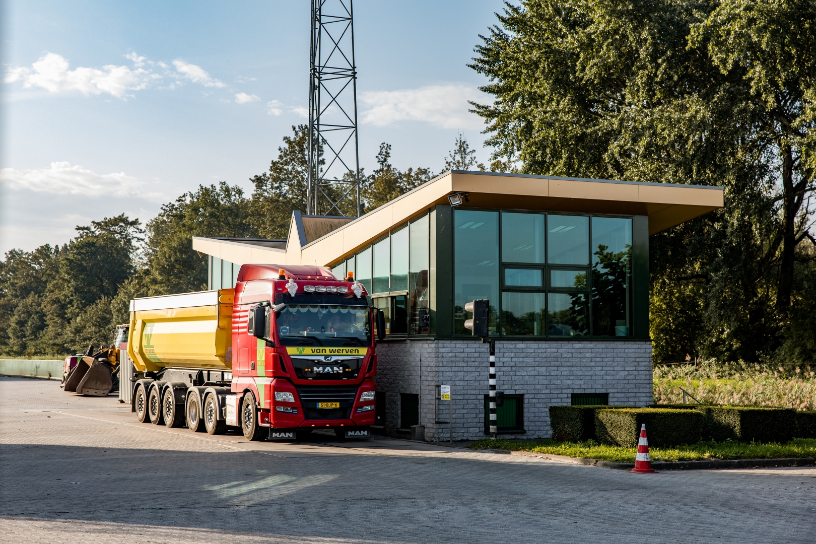 Een rode MAN-vrachtwagen van Van Werven met gele kipoplegger staat op de weegbrug bij het glazen weegkantoor