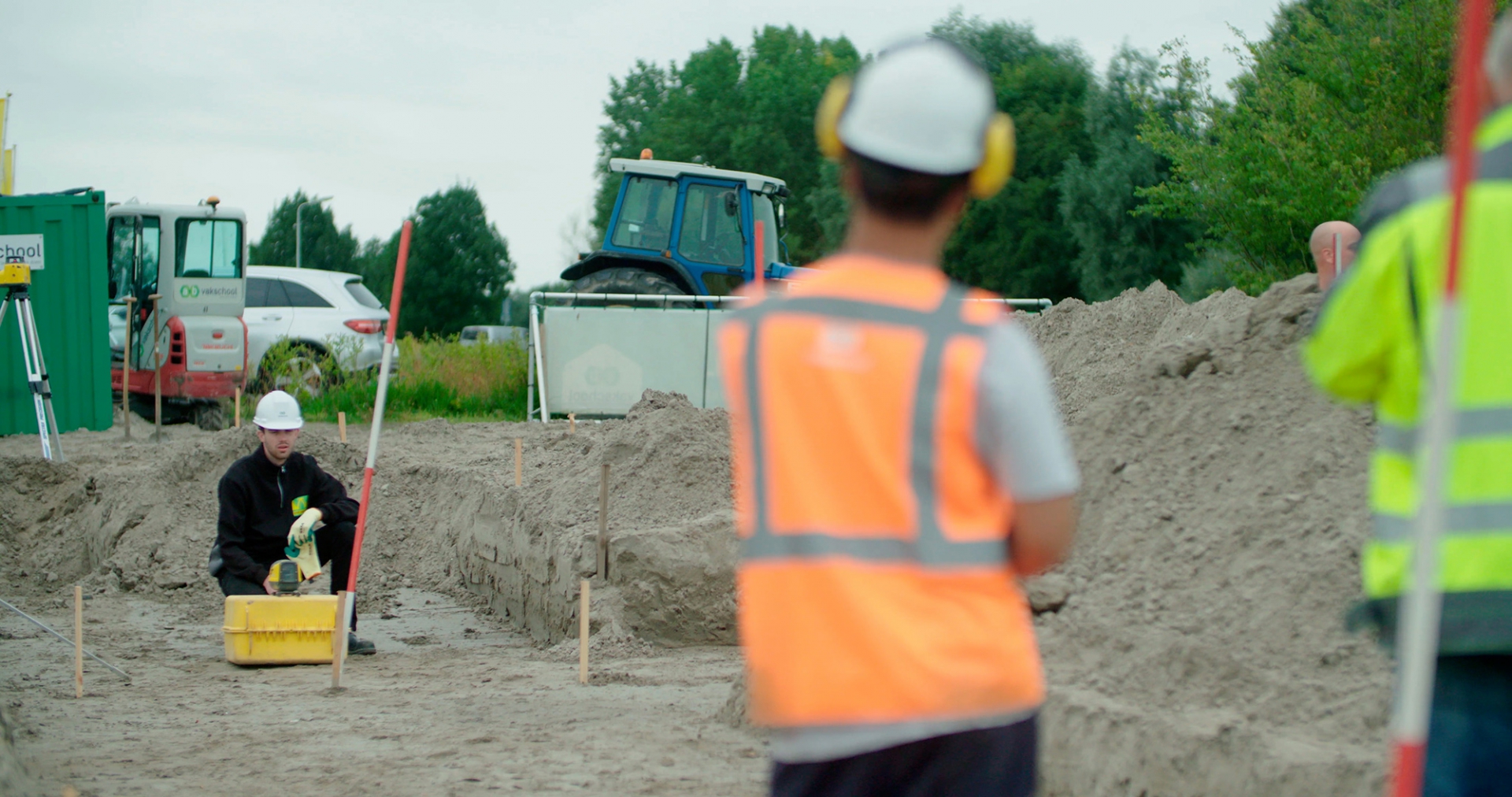 Cursisten in veiligheidshesjes en helmen aan het werk in een uitgegraven bouwput tijdens een praktijkopleiding