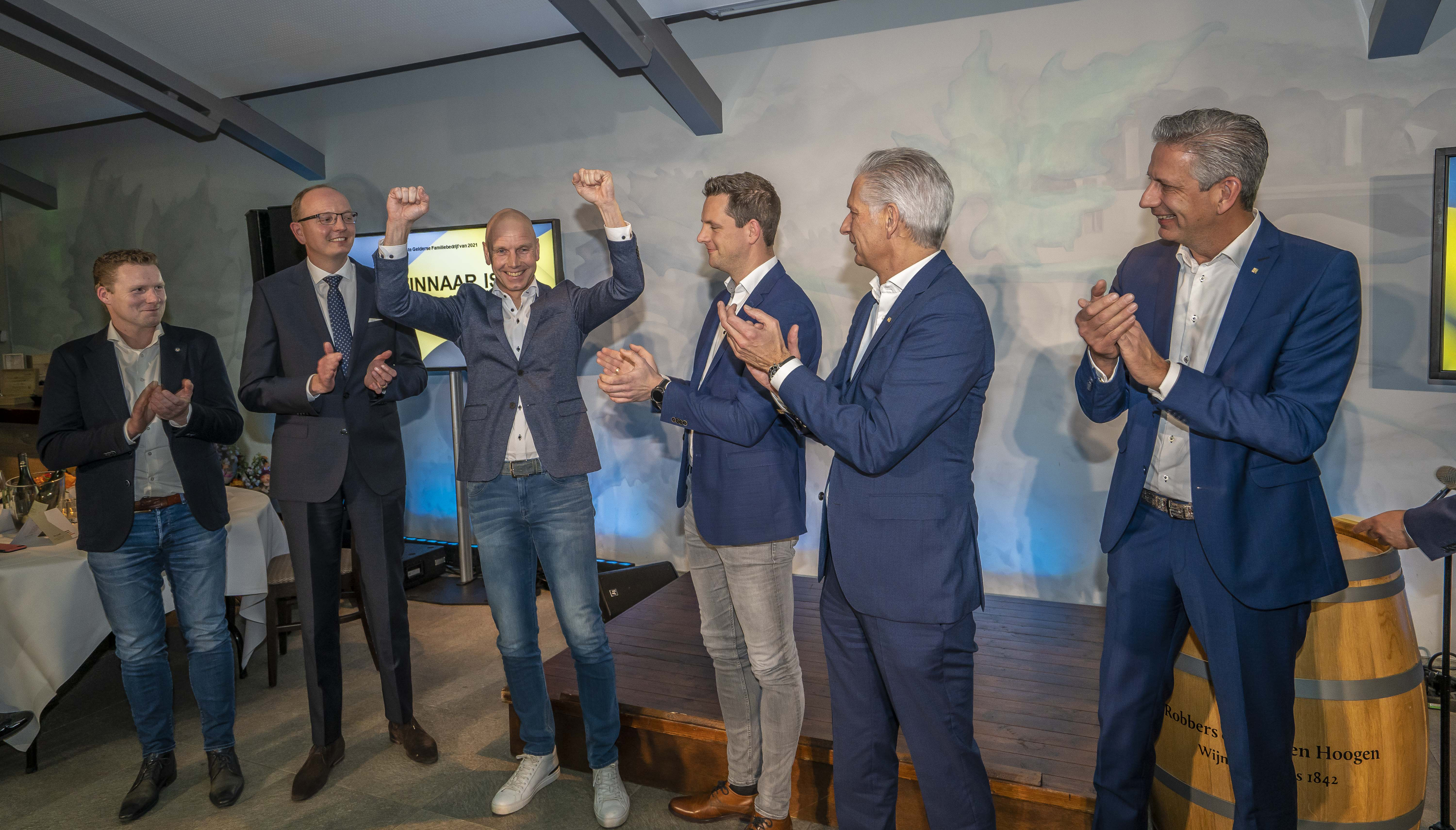 Feestelijk moment bij de bekendmaking: een man juicht met gebalde vuisten terwijl omstanders applaudisseren