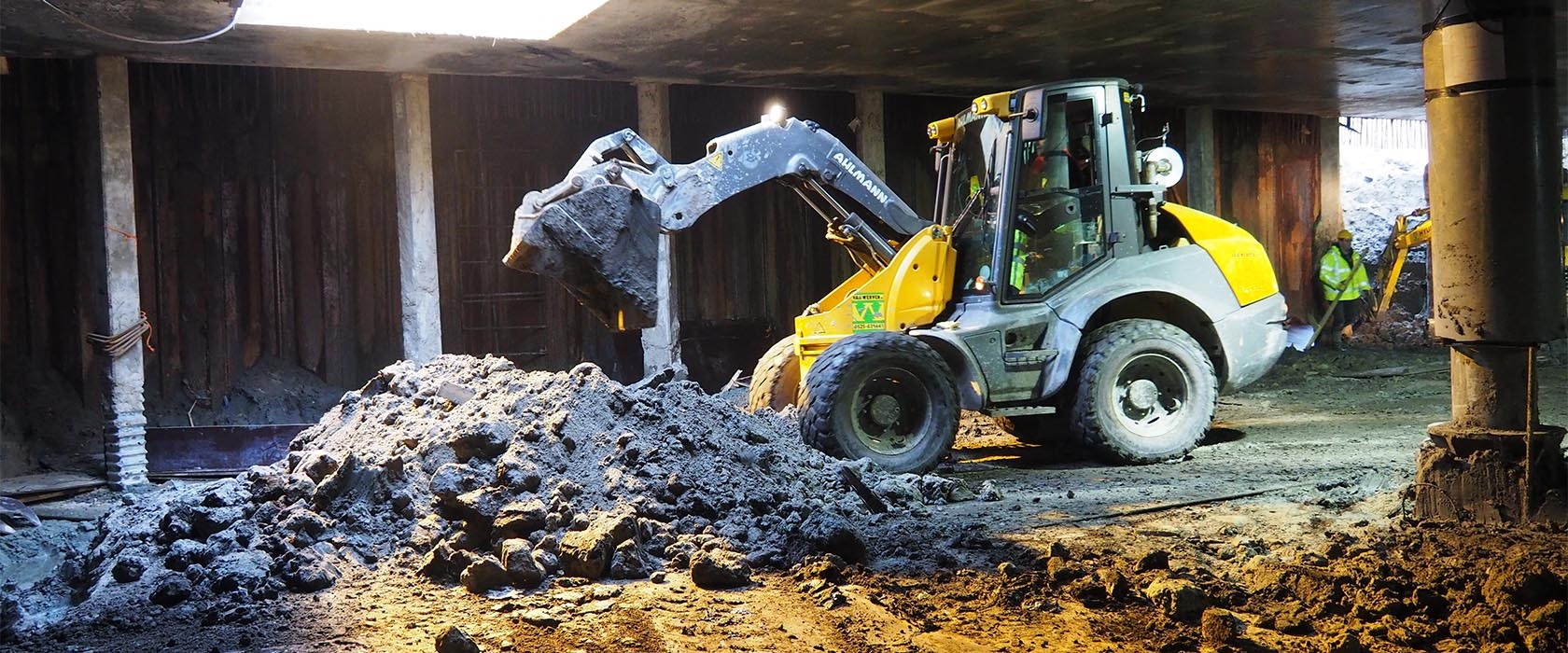 Een gele shovel van Van Werven schept puin onder het betonnen dek van de nieuwe fietsenkelder