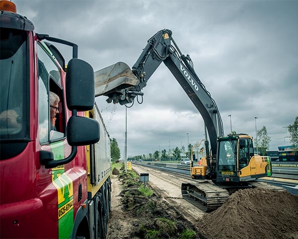 De chauffeur kijkt vanuit zijn cabine toe hoe de graafmachine zijn wagen laadt