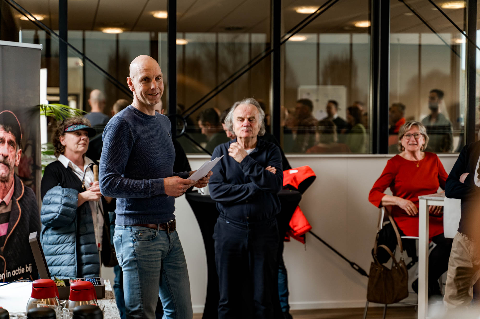 Een spreker met een vel papier richt zich tot de genodigden in de ontvangstruimte