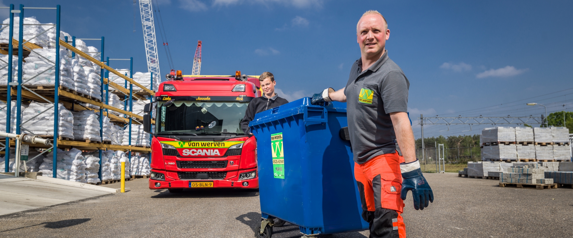 Medewerker rijdt een blauwe rolcontainer weg voor de rode Scania-kraakperswagen
