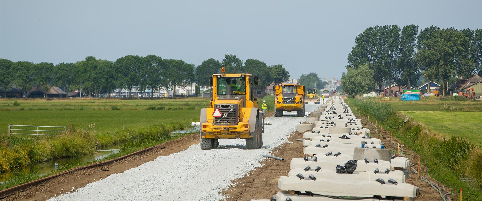 Een wiellader en een dumper van Van Werven rijden over het verse ballastbed langs het spoor, met stapels betonnen dwarsliggers ernaast
