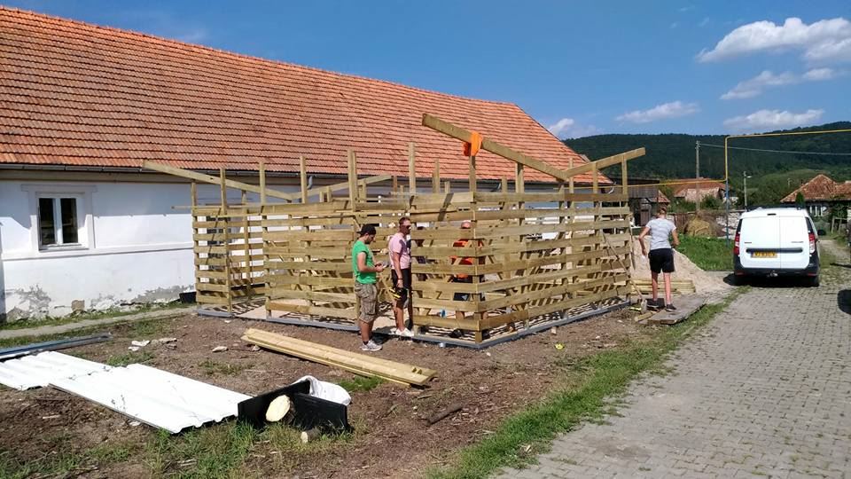 Vrijwilligers bouwen een constructie van houten latten naast een wit huis in Roemenië