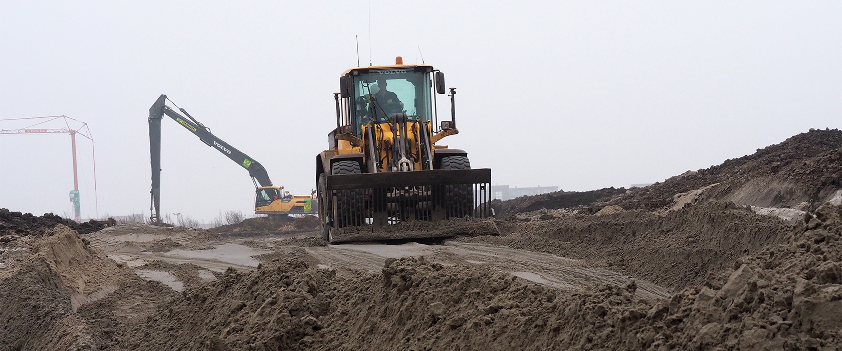 Een Volvo-shovel van Van Werven duwt zand over het natte zandlichaam, met een rupskraan met lange giek in de nevel erachter